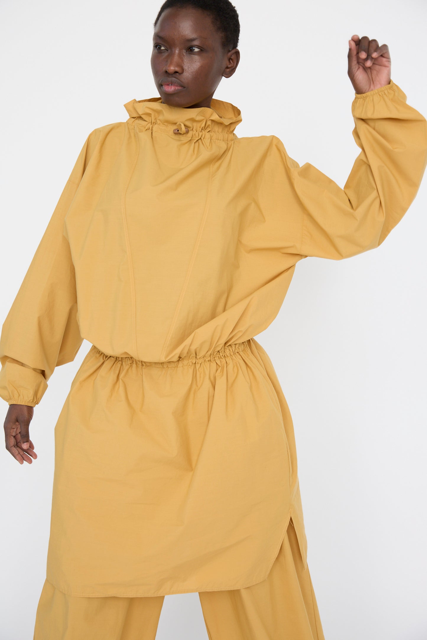 A person is wearing a loose-fitting Baserange Cotton Poplin Air Dress in Sighs Yellow, standing with one arm raised.