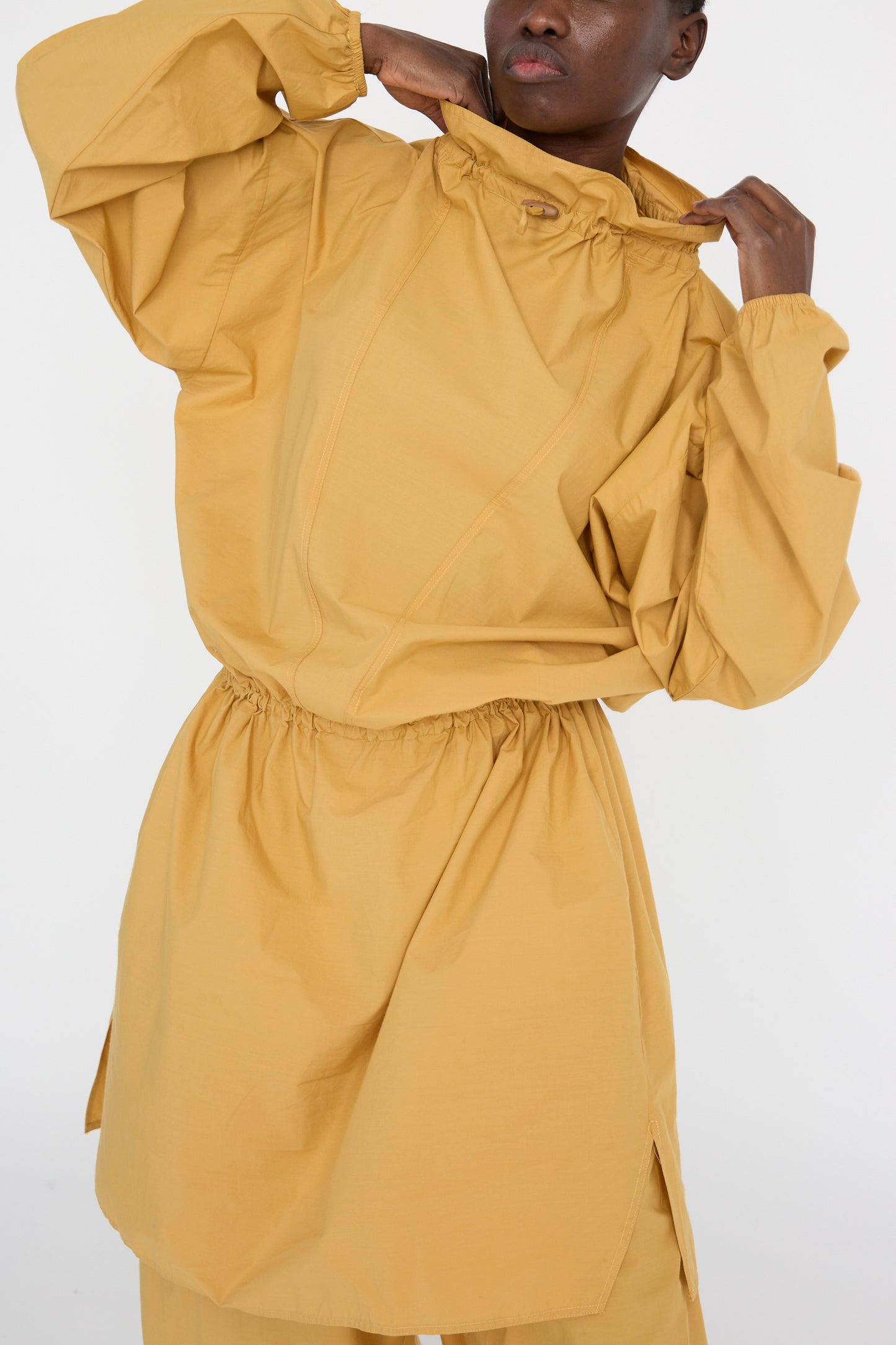 The model is wearing the Baserange Cotton Poplin Air Dress in Sighs Yellow, featuring a loose-fitting, oversized design with a cinched waist and long sleeves, set against a plain background.