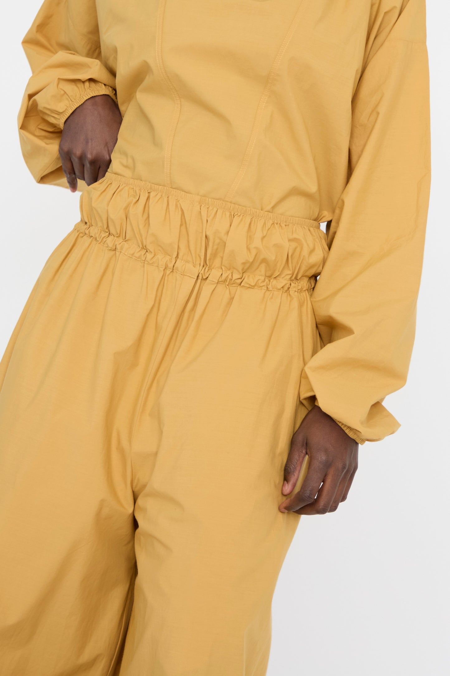 A person is shown neck down in Baserange's Cotton Poplin Air Pants in Sighs Yellow—featuring balloon legs and an elastic waistband made from organic cotton, set against a plain background.