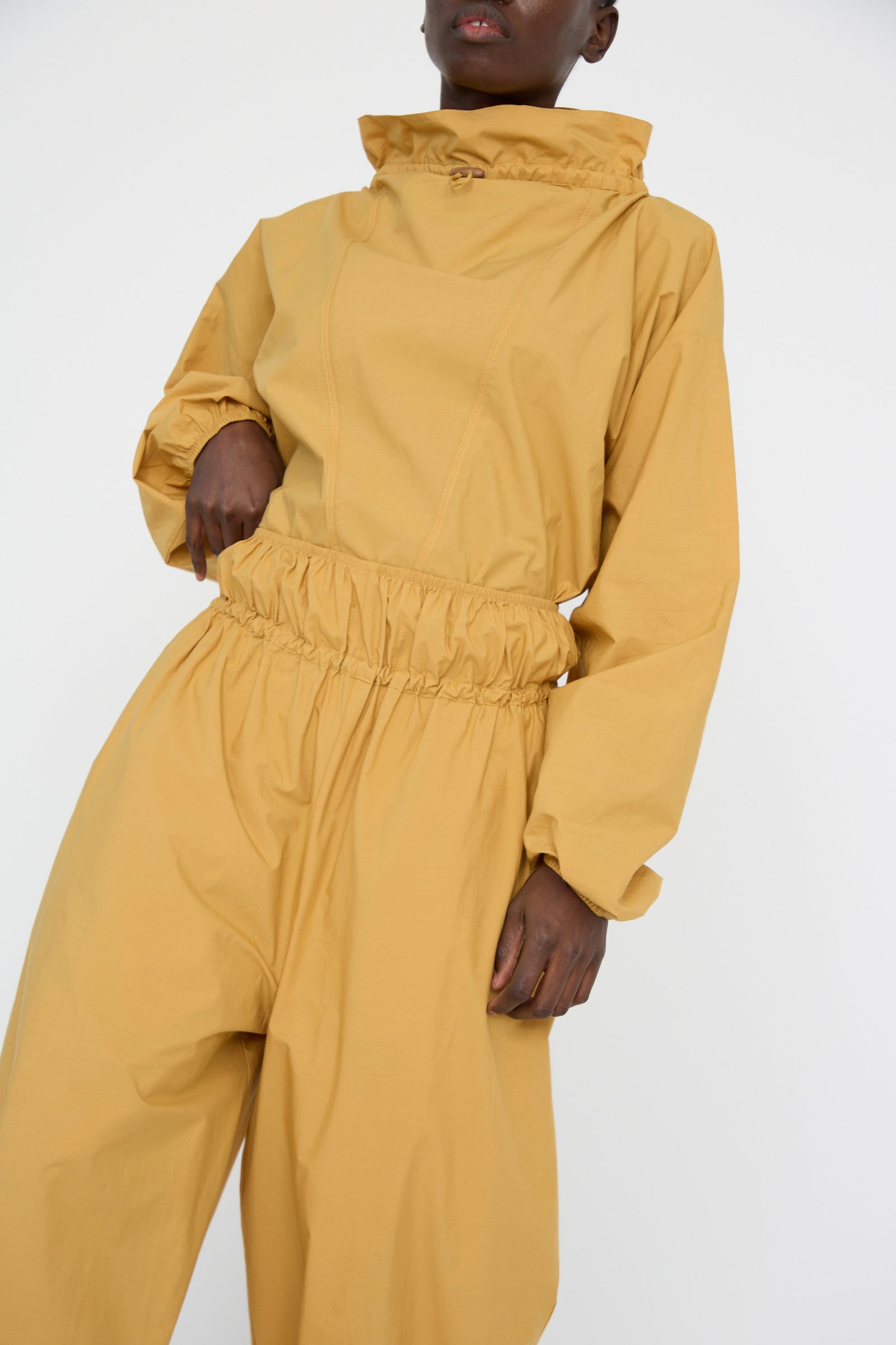 Against a plain background, a person models the Baserange Cotton Poplin Air Pants in Sighs Yellow, with matching top. 