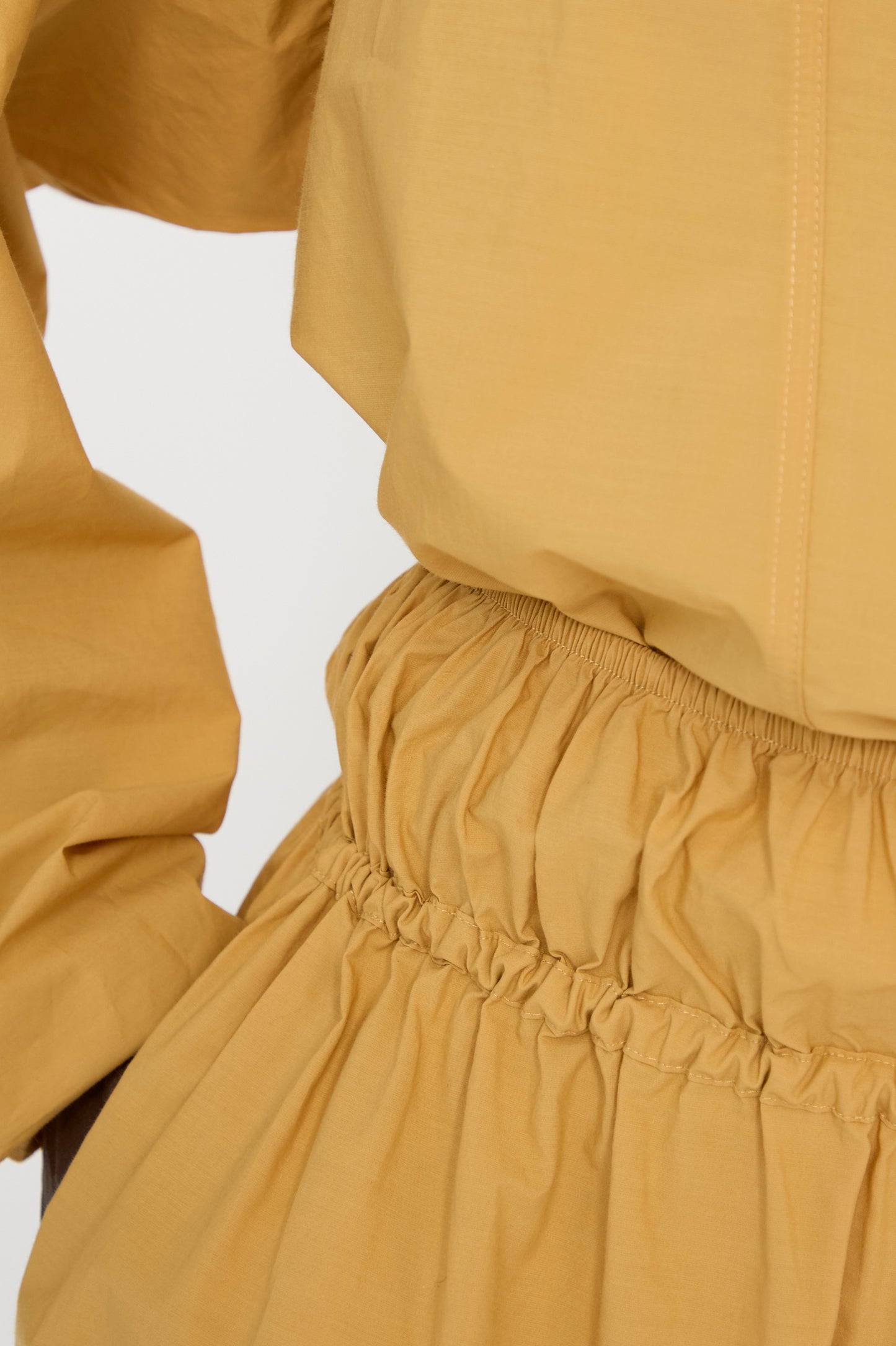 Close-up of a person wearing the Baserange Cotton Poplin Air Pants in Sighs Yellow. Made from organic cotton with an elastic waist. 