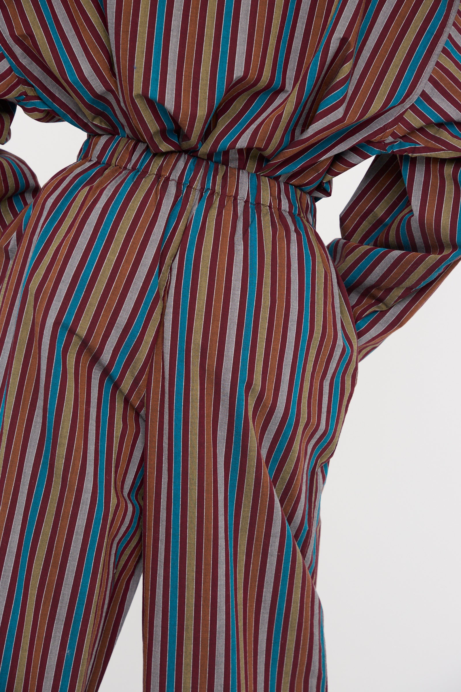 The Baserange Cotton Poplin Ole Pants in Maroon Multi Stripe, crafted from organic cotton, showcase vertical red, blue, green, and brown lines, close up against a white backdrop. 