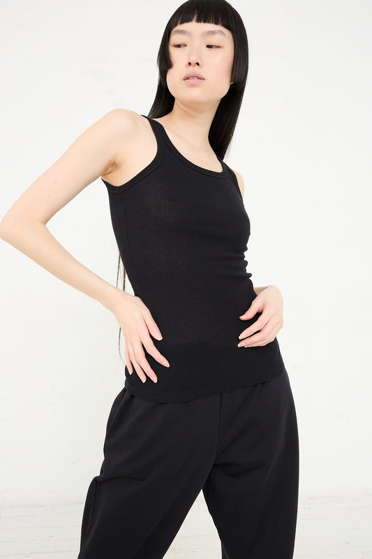 A young Asian woman in a Baserange Organic Cotton Rib Drive Tank in Black and loose black trousers poses against a plain white background.