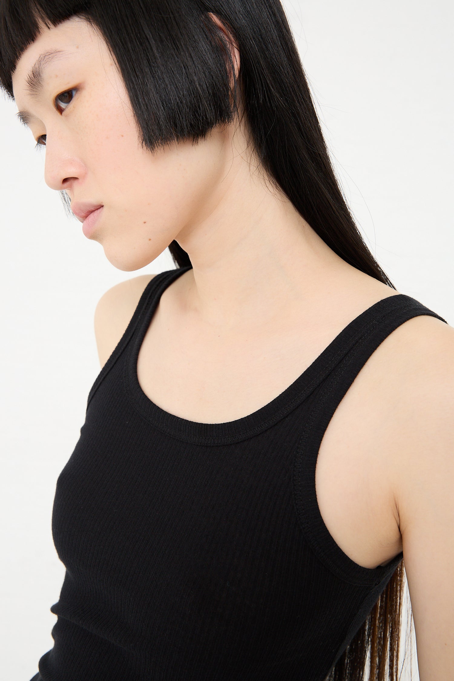 Woman with a bob haircut wearing a Baserange Organic Cotton Rib Drive Tank in Black, profile view.