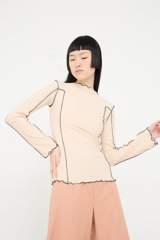 Asian woman with a bob haircut poses in a Baserange Organic Cotton Rib Omato Long Sleeve in Kano Pink top and peach trousers against a white background.