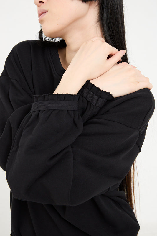 Woman in a Baserange Organic Cotton Route Sweatshirt in Black, touching her shoulder with a thoughtful pose, white background.