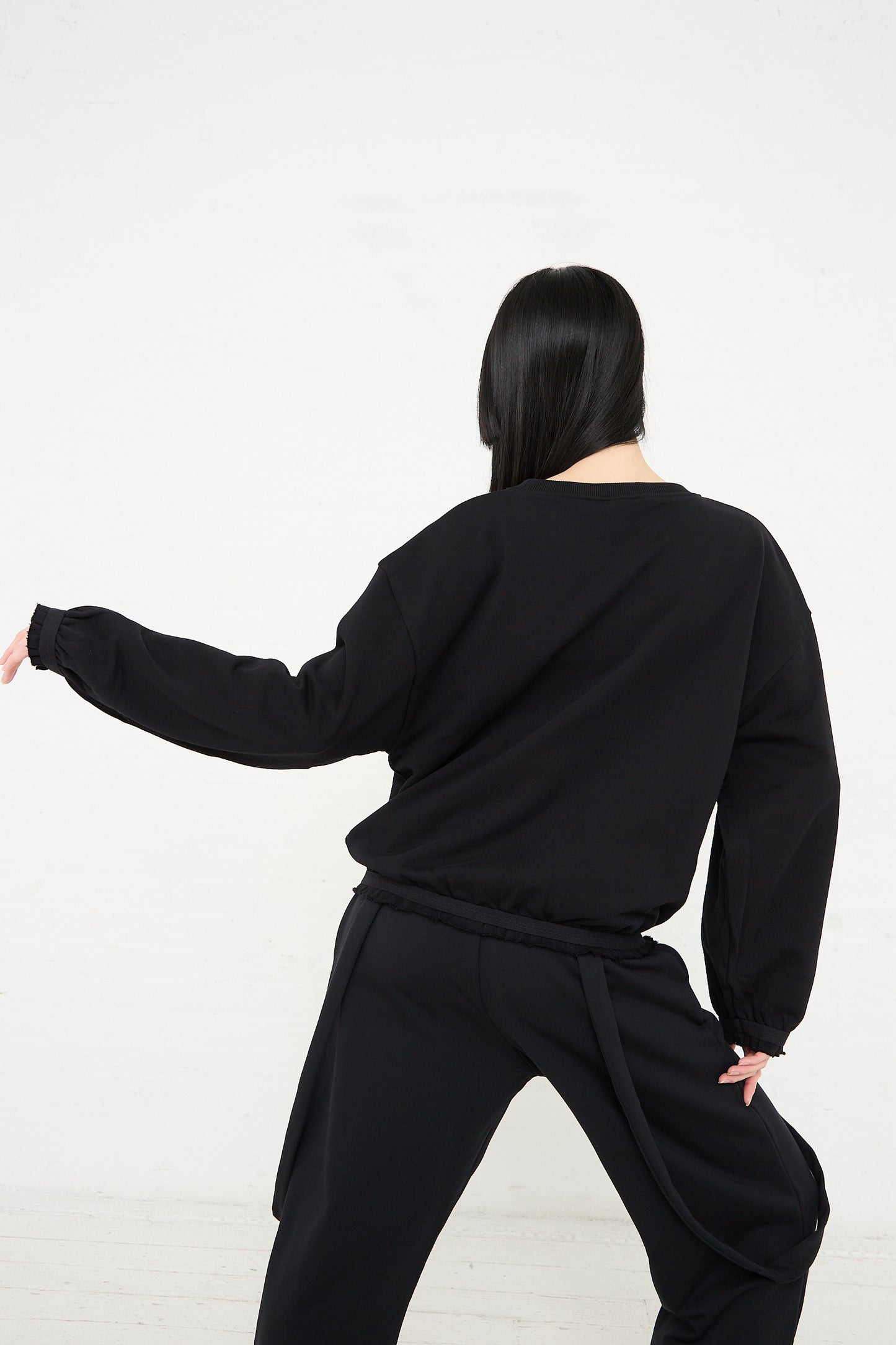 Woman in Baserange Organic Cotton Route Sweatshirt in Black performing a martial arts stance against a white background.