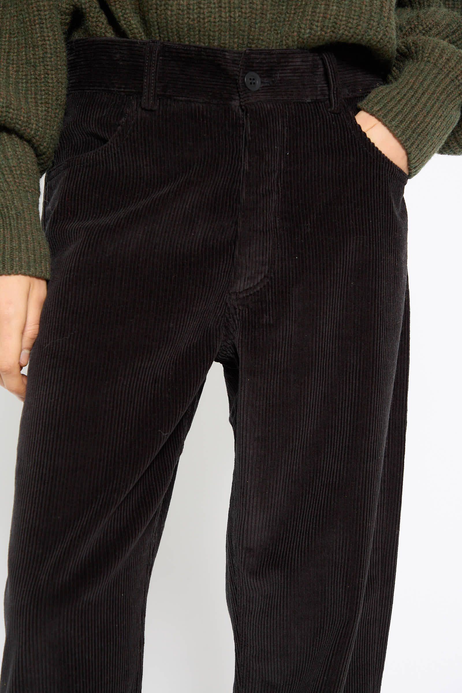 Close-up of a person wearing relaxed fit, Baserange Cotton Tajo Pant in black and a green ribbed sweater with one hand in a pocket.