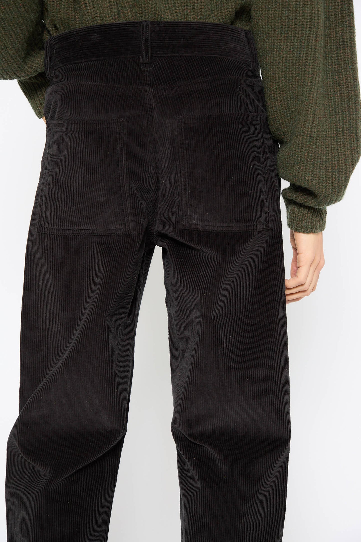 A person wearing a green sweater and the Baserange Cotton Tajo Pant in Black is shown from the back, with a focus on the waist and pockets of the high-rise pants.