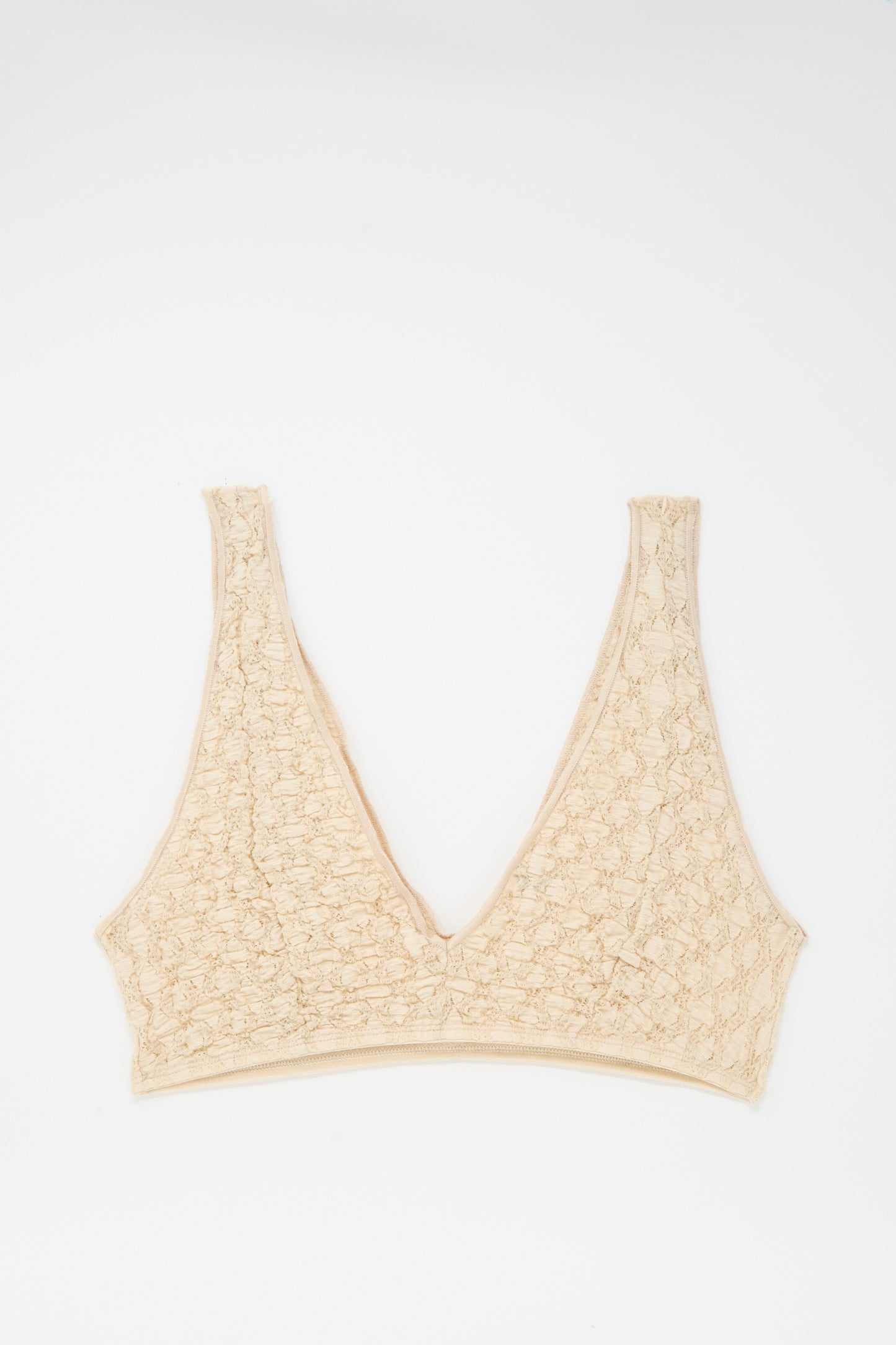 The Crescent Bra in Dylan Beige by Baserange features a textured V-neck, wide straps, and elastic trim, shown laid flat on a white background.