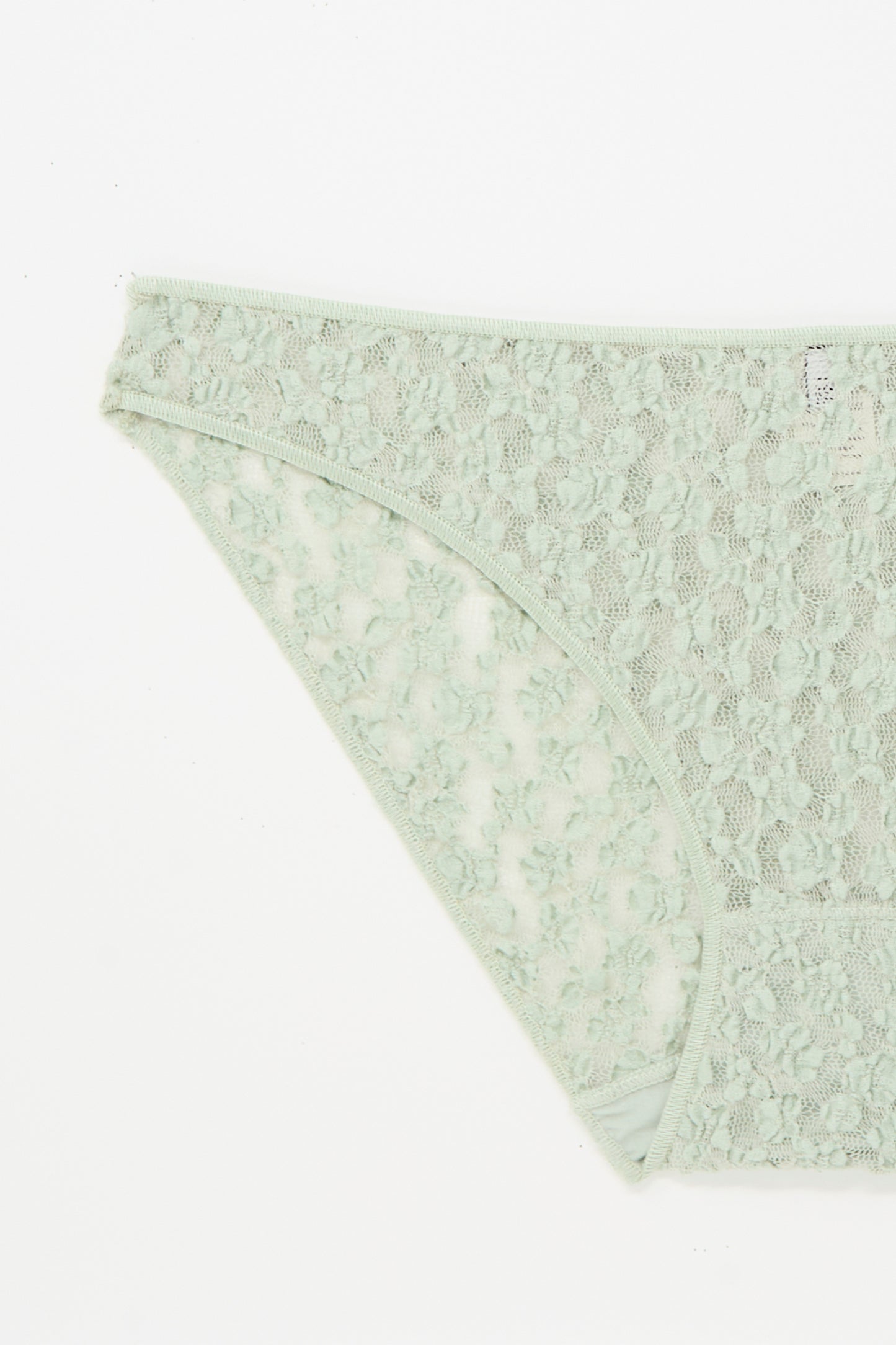 A close-up of the Baserange Crescent Pants in Conta Green, an organic cotton lace brief, laid flat on a white background.