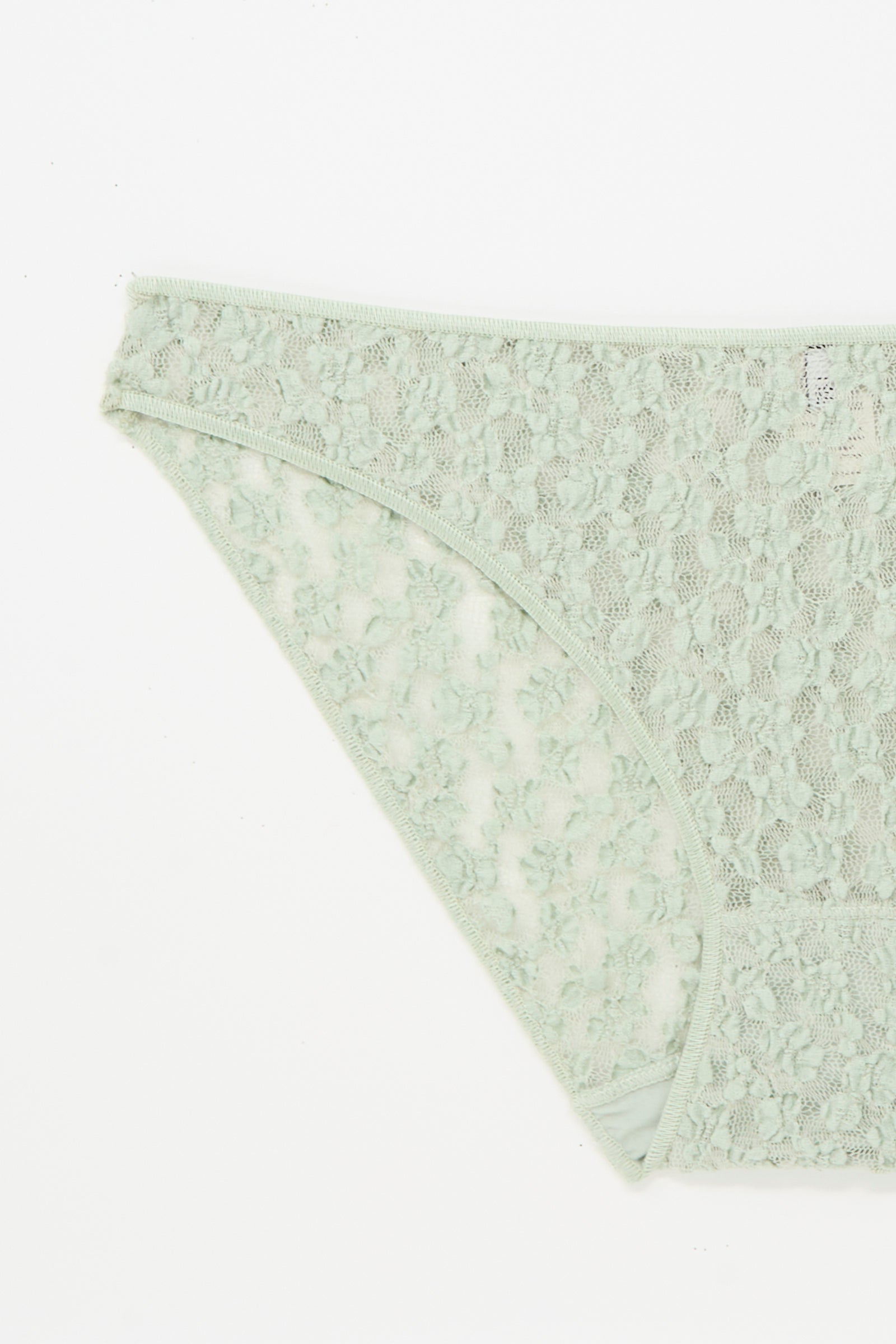 A close-up of the Baserange Crescent Pants in Conta Green, an organic cotton lace brief, laid flat on a white background.