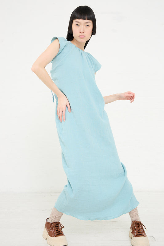 Woman posing in a Crinkle Linen Cotton Max Dress in Wuxi Blue made from organic cotton by Baserange with casual sneakers.