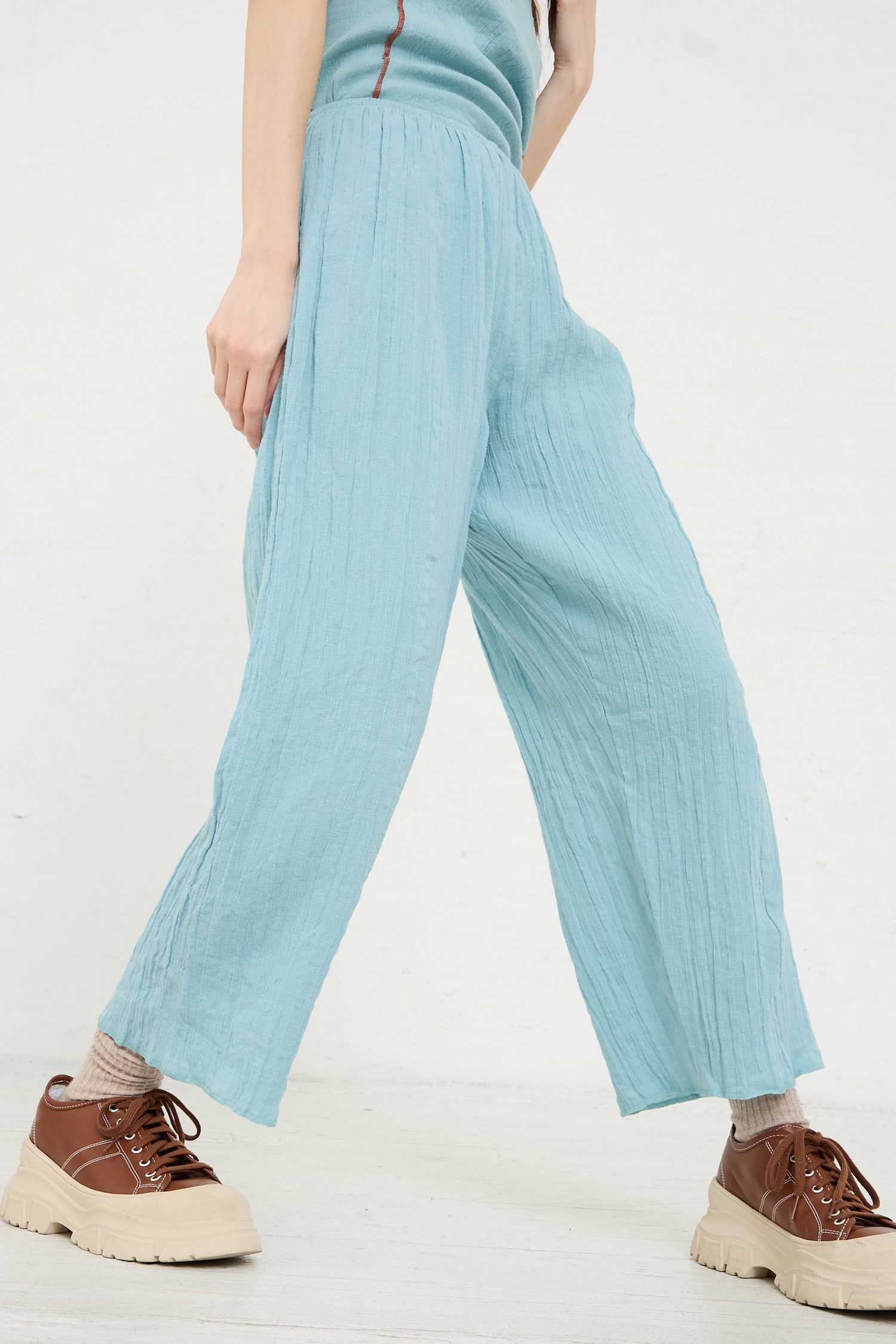 A person standing in a light blue pair of Crinkle Linen Cotton Shok Pants in Wuxi Blue by Baserange and brown lace-up shoes.