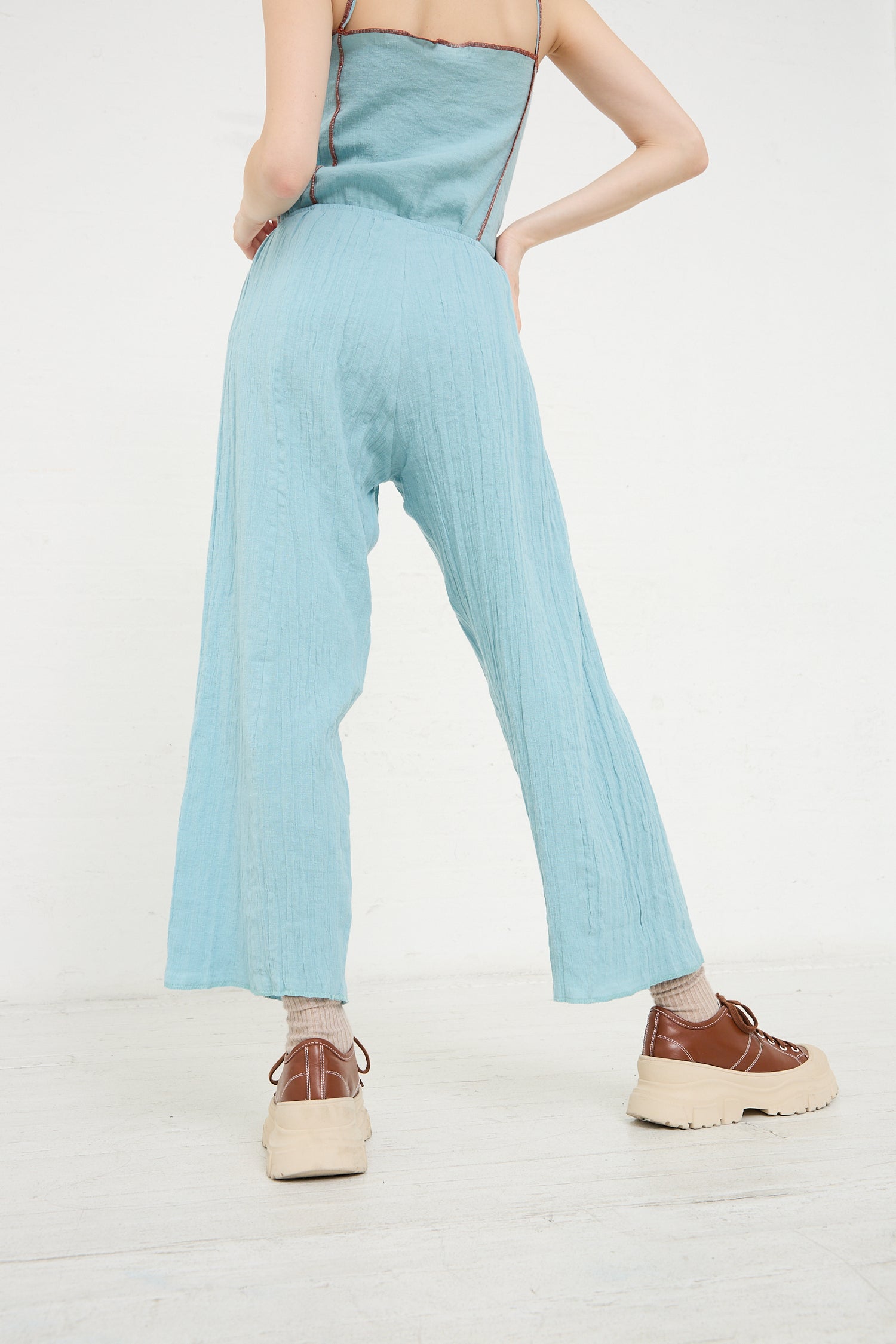Person wearing the Baserange Crinkle Linen Cotton Shok Pant in Wuxi Blue and chunky brown shoes viewed from the back.