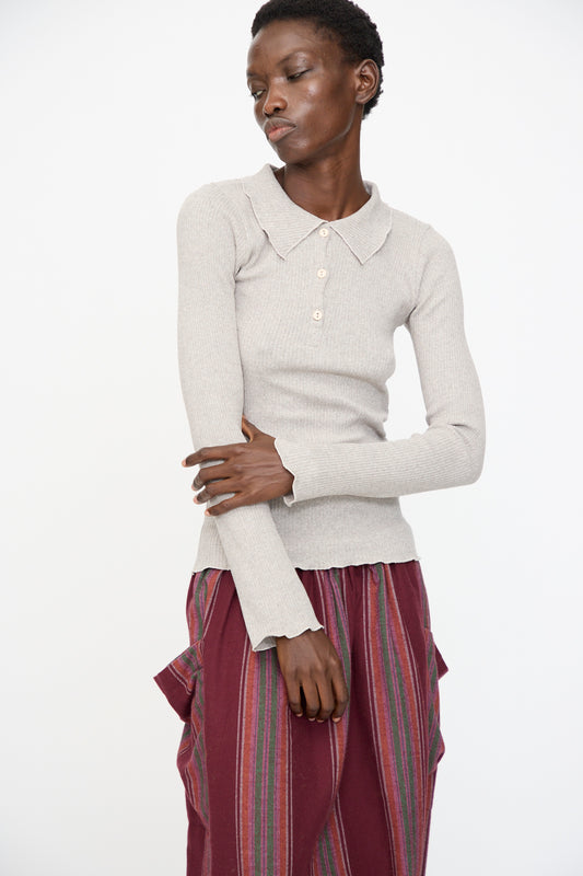 A person wears the Baserange Dual Long Sleeve Tee in Grey Melange, styled with a burgundy striped skirt with side pockets, standing against a plain white background.