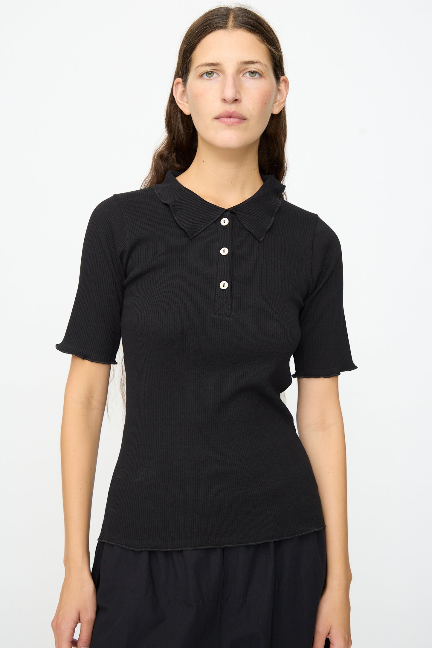 A person with long brown hair wears the Baserange Dual Polo in Black, featuring a slim fit, three buttons, and a collar, standing against a plain white background.