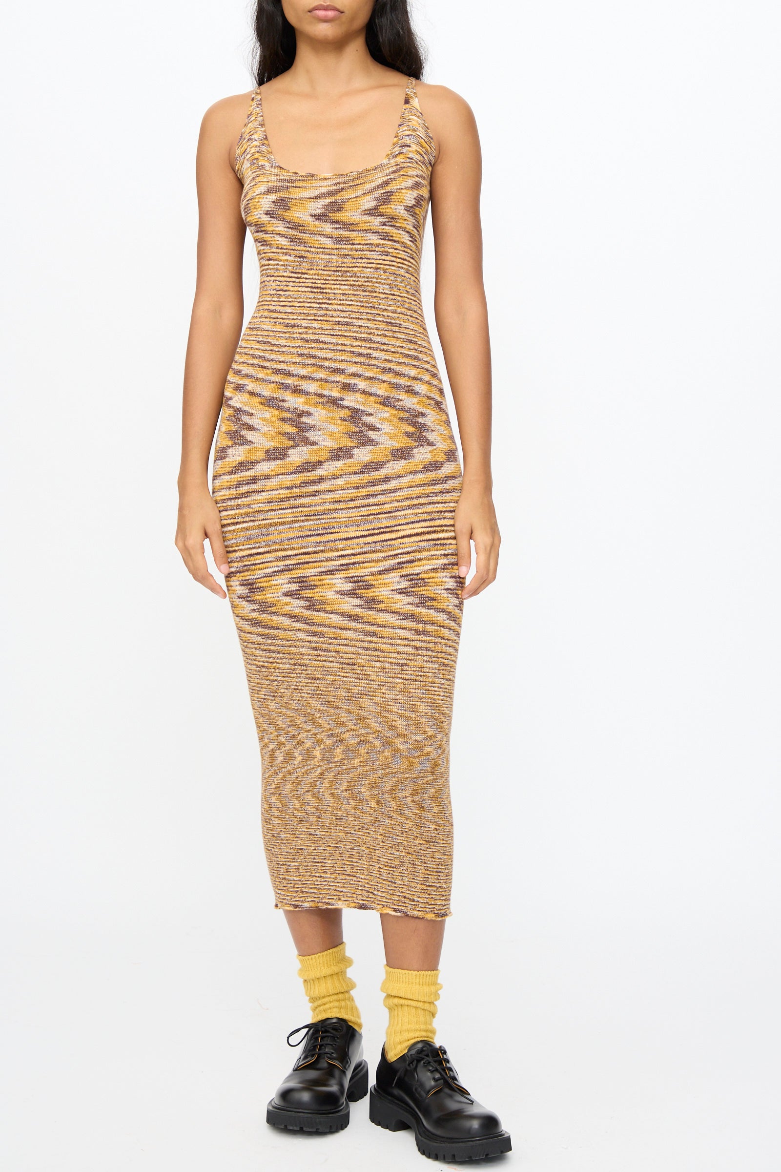 A woman wears the Flute Dress in Brown Melange by Baserange, a sleeveless slim-fit midi dress, styled with yellow socks and black lace-up shoes.