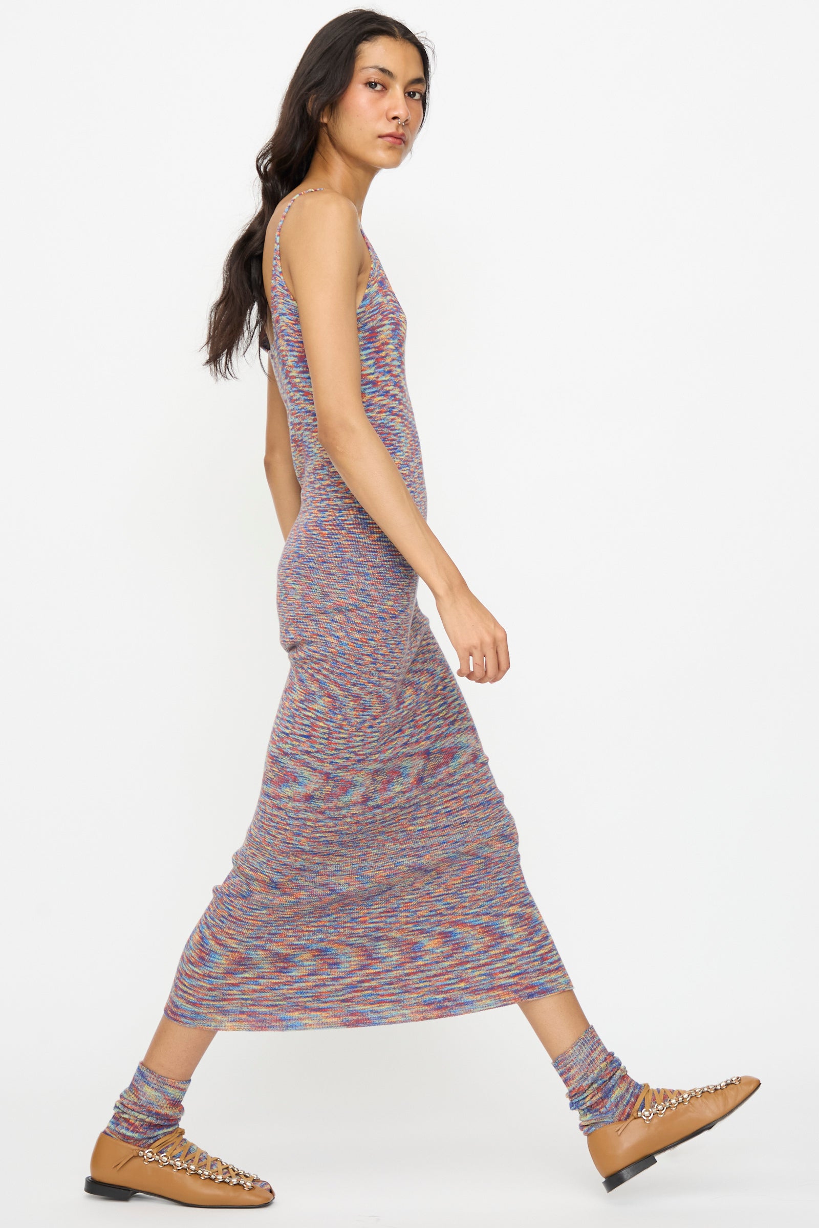 Model wearing the Baserange Flute Dress in Multicolored, paired with matching socks and tan woven shoes, walks in profile against a plain white background.