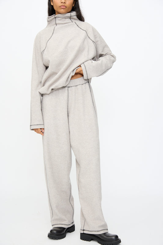 Person wearing Baserange Fold Sweatpant in Grey Melange, a relaxed fit wide-leg sweatpant made from recycled cotton, paired with a matching sweatshirt and black shoes, standing against a plain white background.