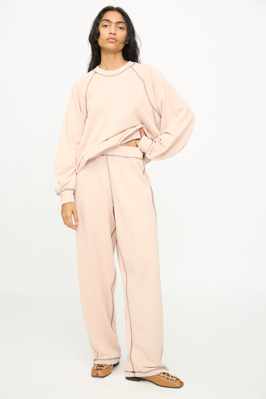 A person stands in a relaxed pose wearing Baserange’s Fold Sweatpants in Haptic—a loose, light beige cotton blend style with an elastic waistband—paired with a matching sweatshirt and tan flat shoes against a plain white background.