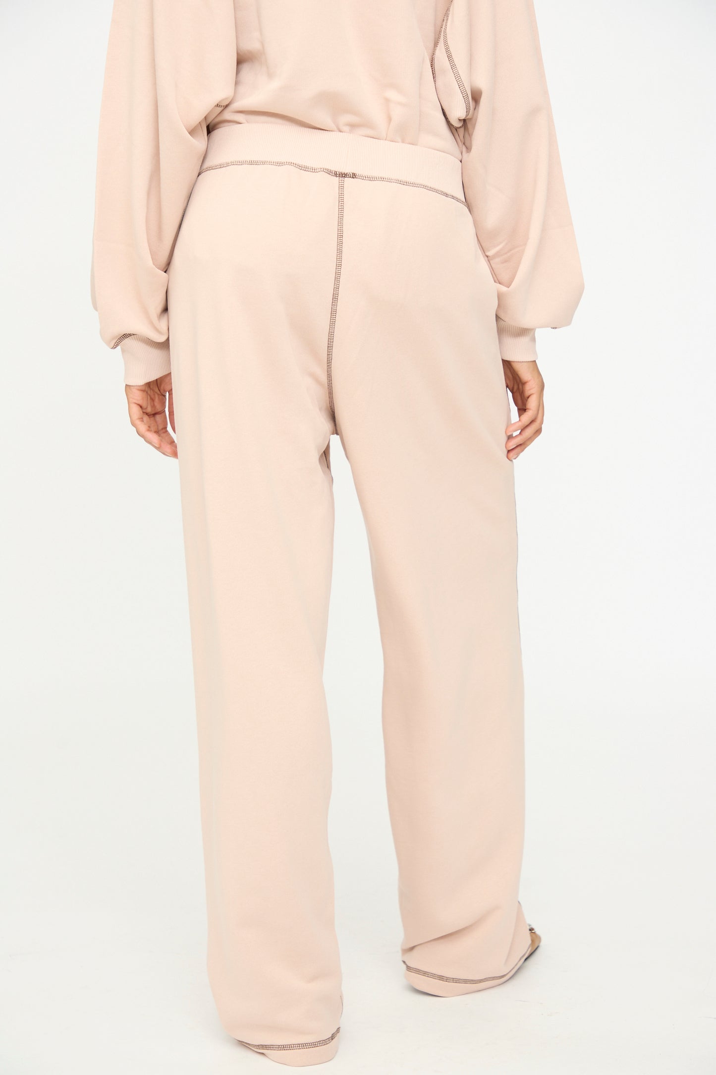 A person is shown from the back against a plain white background, wearing Baserange’s Fold Sweatpants in Haptic—a loose-fitting, light beige cotton blend style with an elastic waistband—paired with a matching long-sleeve top.