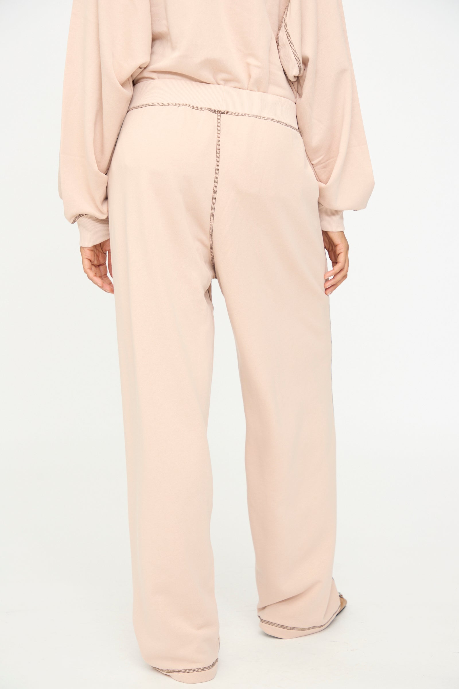 A person is shown from the back against a plain white background, wearing Baserange’s Fold Sweatpants in Haptic—a loose-fitting, light beige cotton blend style with an elastic waistband—paired with a matching long-sleeve top.