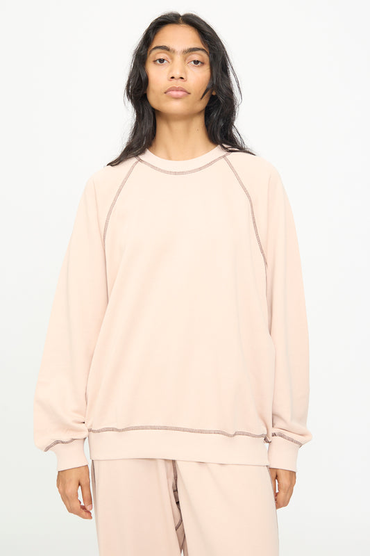 A person with long dark hair wears the Baserange Fold Sweatshirt in Haptic—a loose, light beige crewneck sweatshirt with raglan sleeves—paired with matching pants, standing against a plain white background and looking straight at the camera.