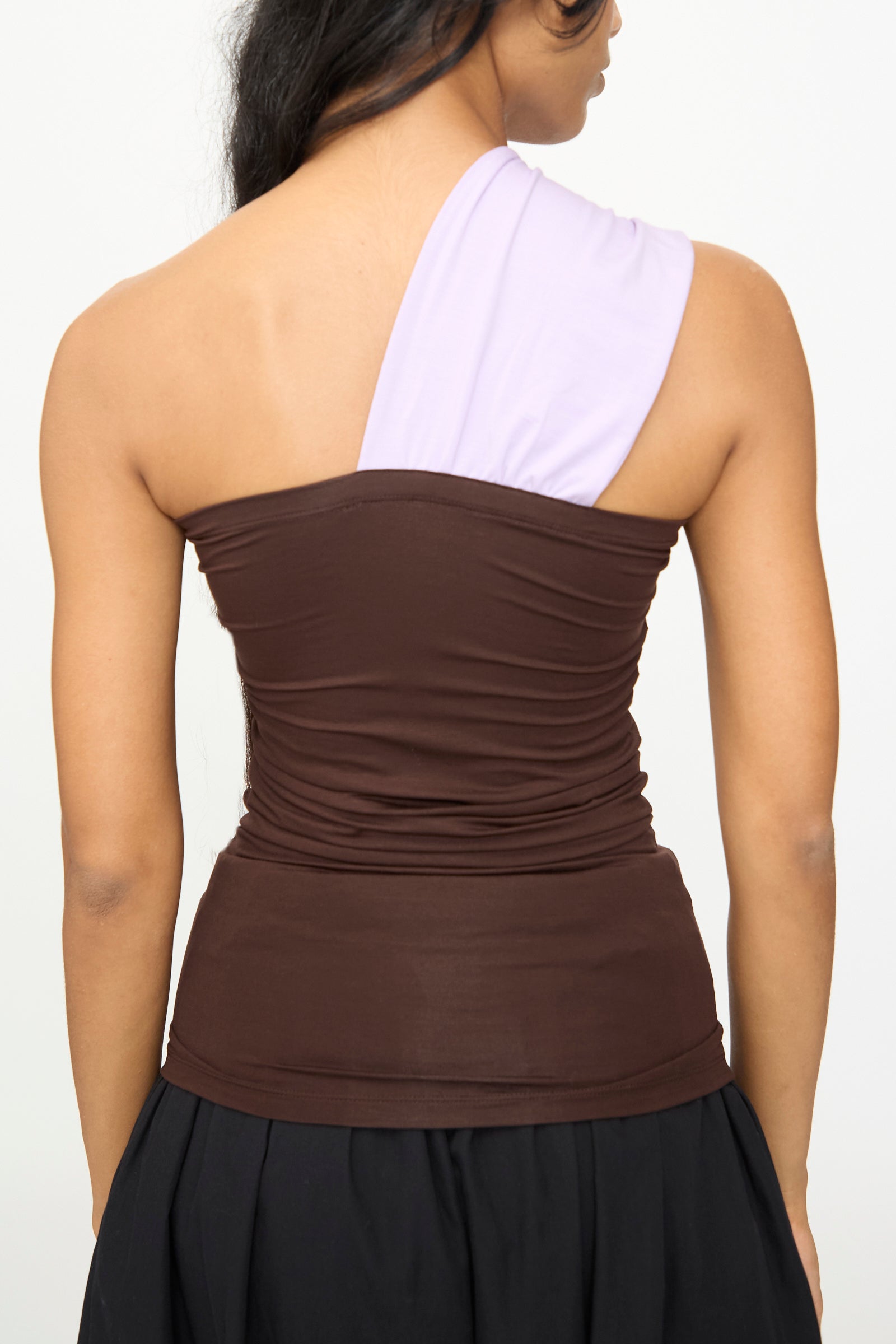 A person seen from the back wearing the Baserange Geo Tank in Tactile One Purple, a brown, asymmetrical one-shoulder top featuring a light purple single shoulder strap.