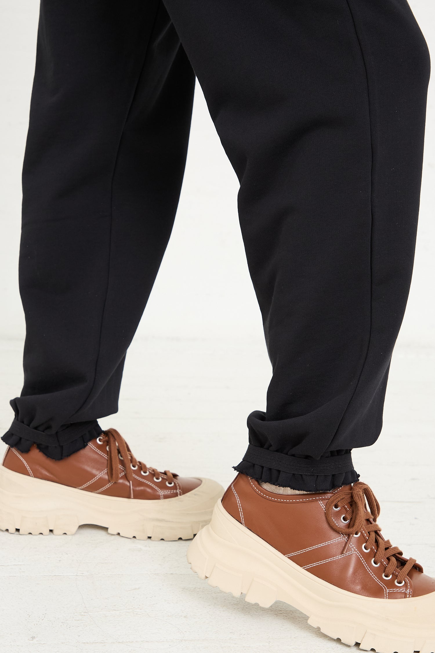 A person standing in Baserange Italian Fleece Route Sweatpants in Black paired with brown lace-up shoes with thick soles.