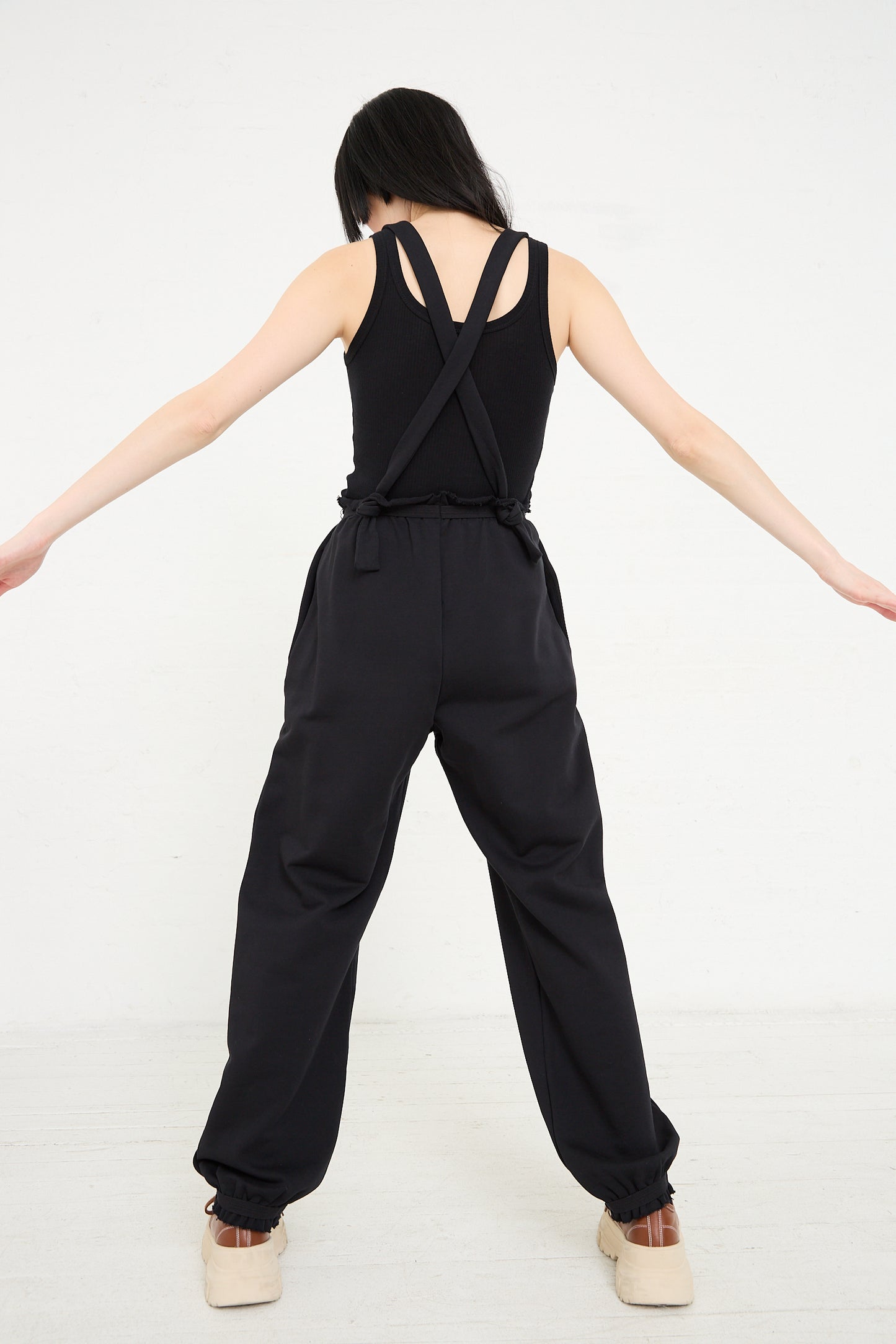 Woman standing with her back turned, wearing a Baserange Italian Fleece Route Sweatpant in Black with relaxed fit, against a white background.