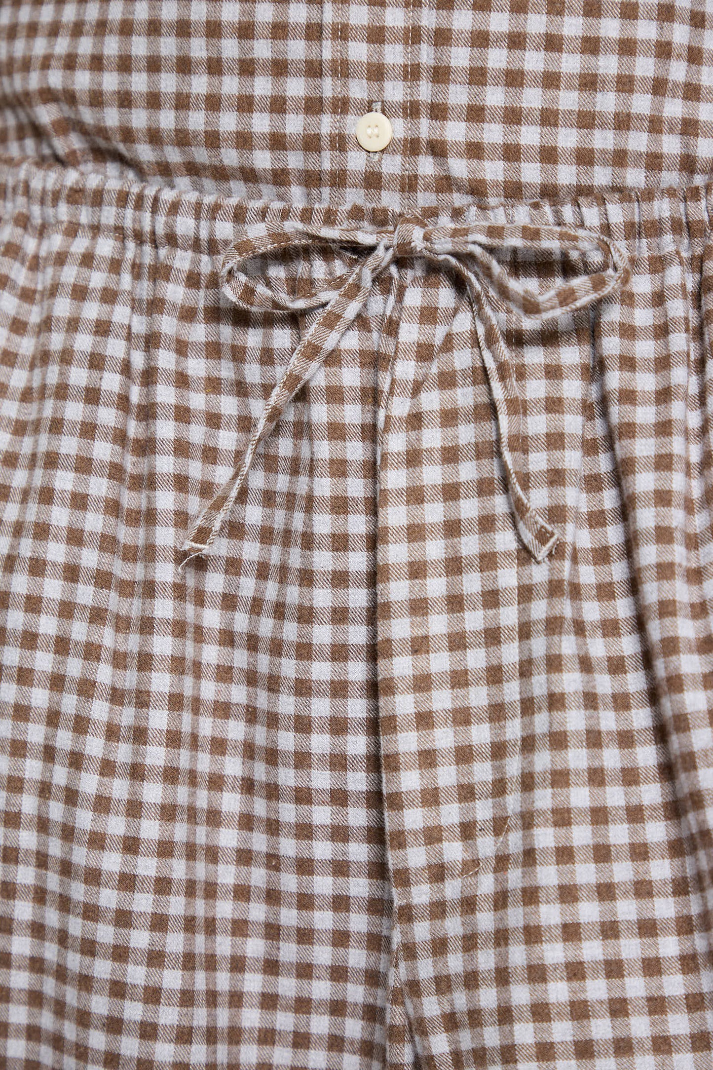 Close-up of the Baserange Limber Pant in Brown Grey Flannel, showcasing a checkered pattern with a drawstring tied in a bow at the center, reminiscent of its relaxed fit design featuring an elasticated waist.