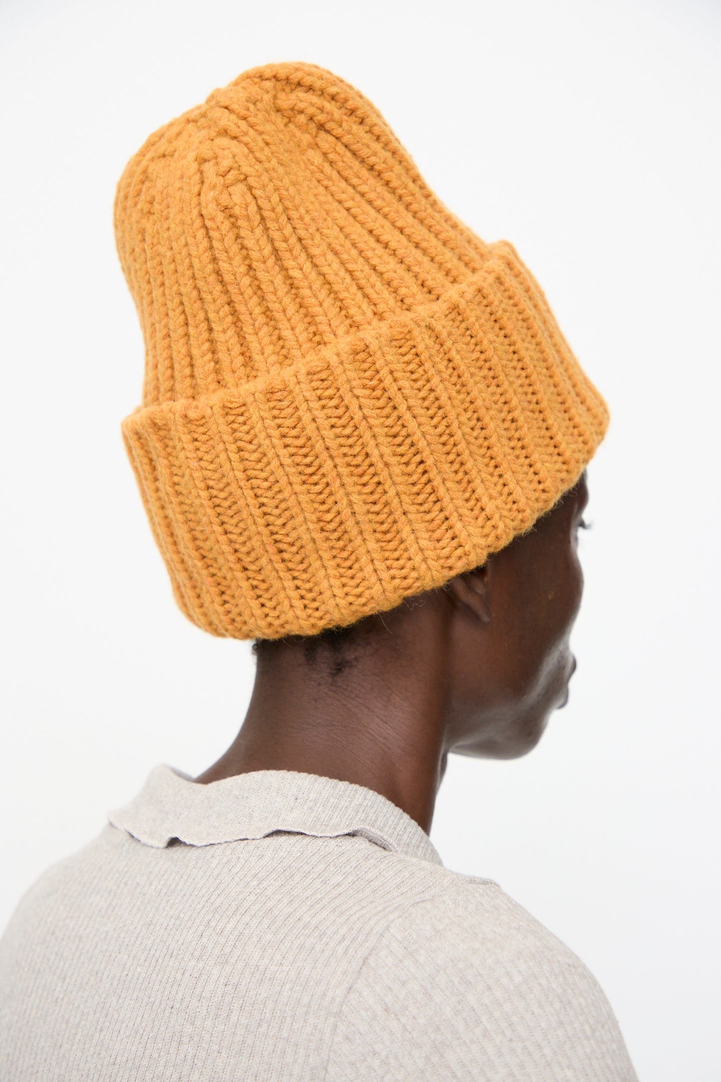 Person wearing the Baserange Mea Beanie in Clair Orange and a beige ribbed shirt, shown from behind against a plain white background.