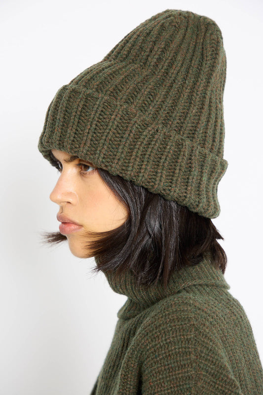 A person wearing the Mea Beanie in Foret by Baserange and a matching chunky ribbed sweater, looking to the side against a plain background.