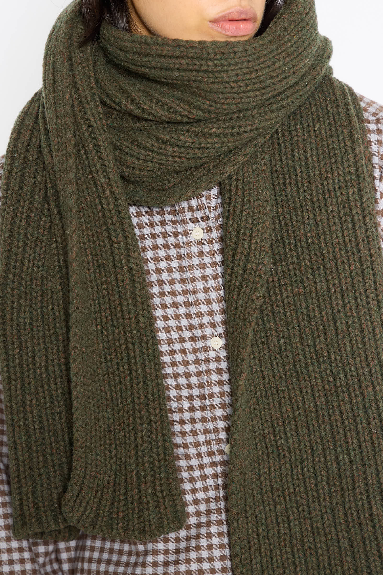 Close-up of a person wearing the Mea Scarf in Foret by Baserange, a chunky knit piece made from a recycled wool blend, paired with a brown and white checkered shirt.