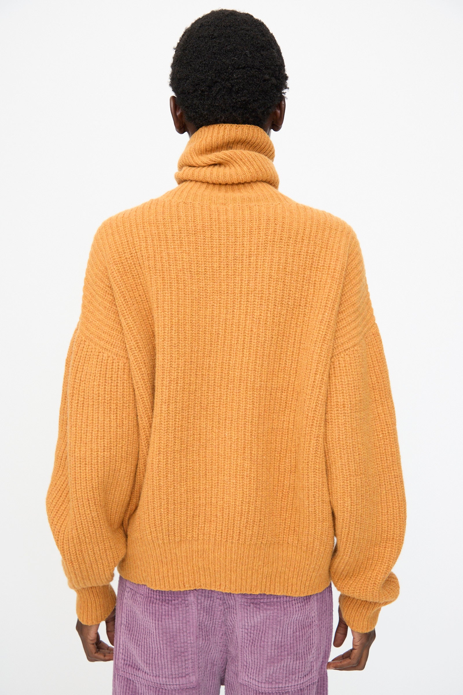 Person facing away from the camera wearing the Baserange Mea Turtleneck in Clair Orange against a plain white background.