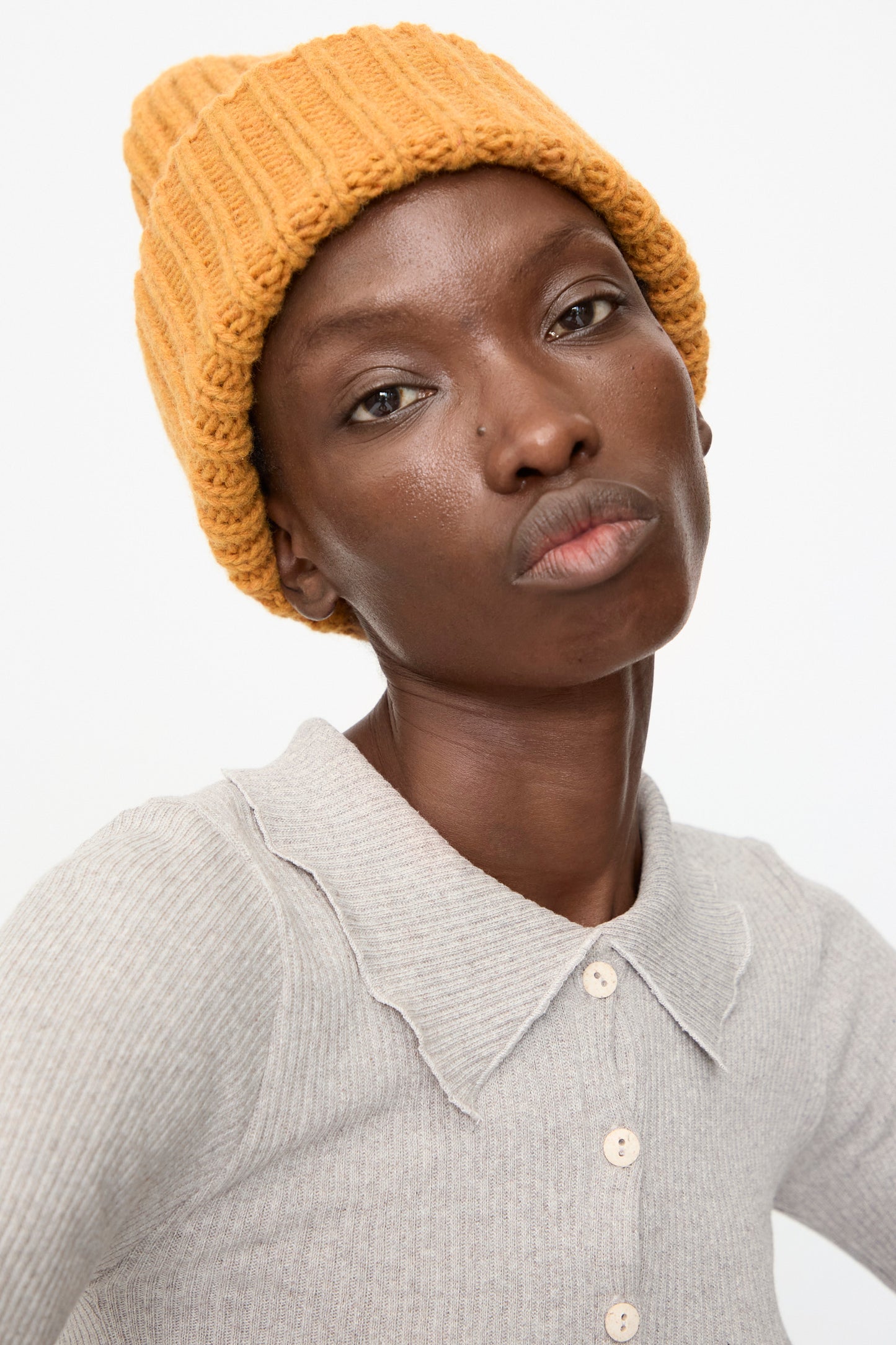 A person wears the Baserange Mea Beanie in Clair Orange and a light grey collared shirt, looking straight at the camera with a neutral expression.