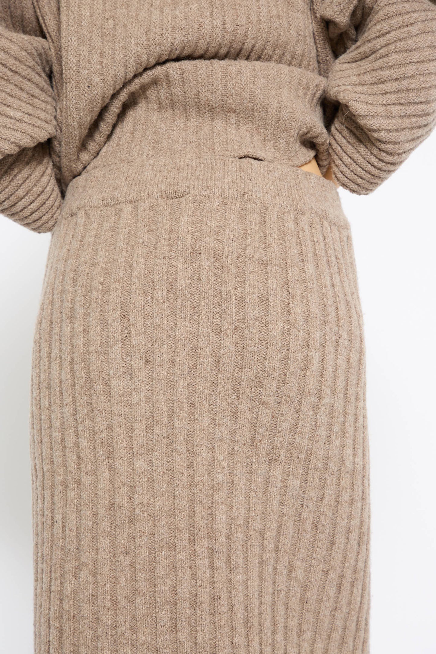 Close-up of a person wearing the Baserange Merino Wool Kai Skirt in Alassio with a matching ribbed, beige, merino wool sweater. The top is slightly tucked into the elasticated waist of the skirt.