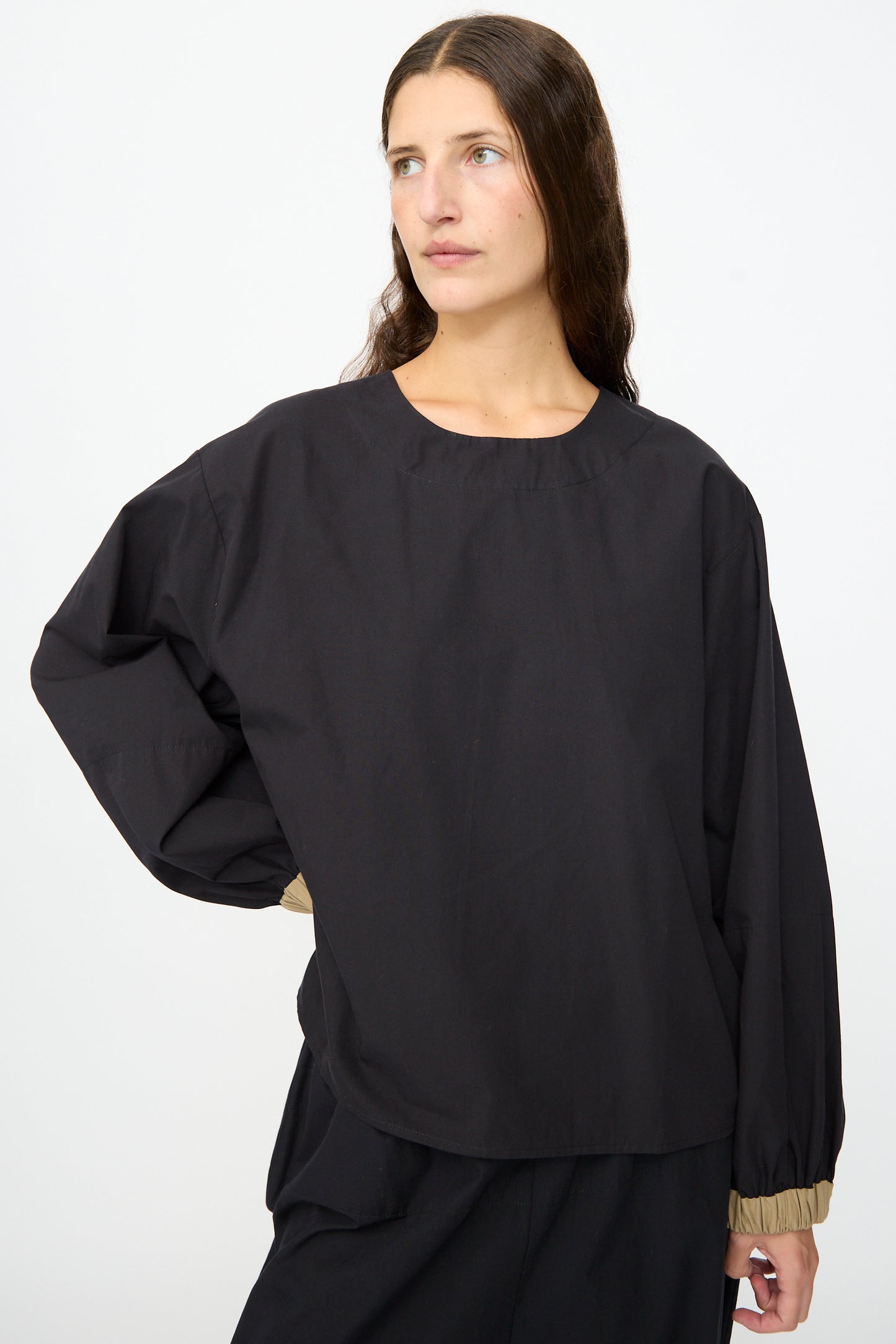 A woman wears the Baserange Moy Top in Black Khaki, styled with matching black pants, standing against a plain white background.