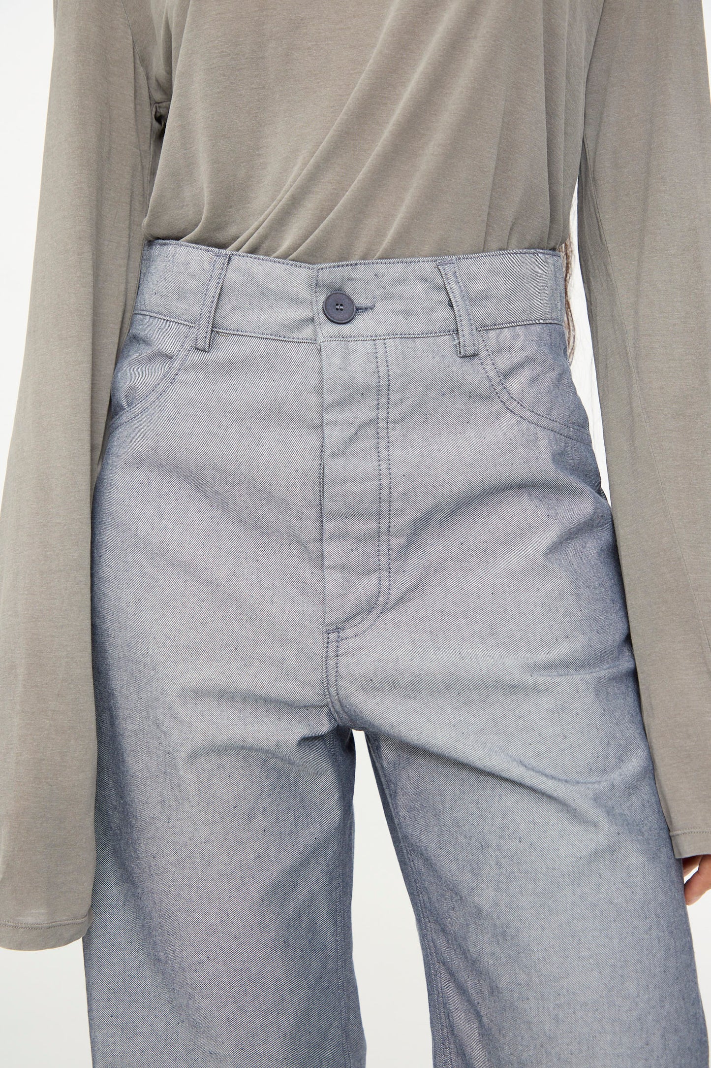 A person wearing a long-sleeved gray top tucked into Baserange’s Navalo Pants in Dark Denim, shown from shoulders to knees.