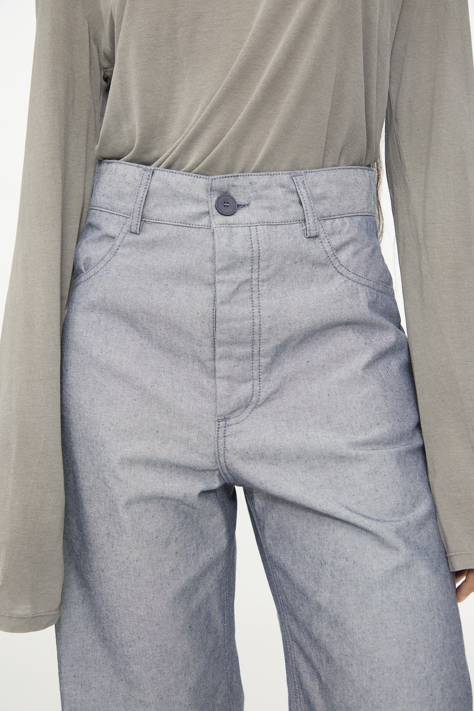 A person wearing a long-sleeved gray top tucked into Baserange’s Navalo Pants in Dark Denim, shown from shoulders to knees.