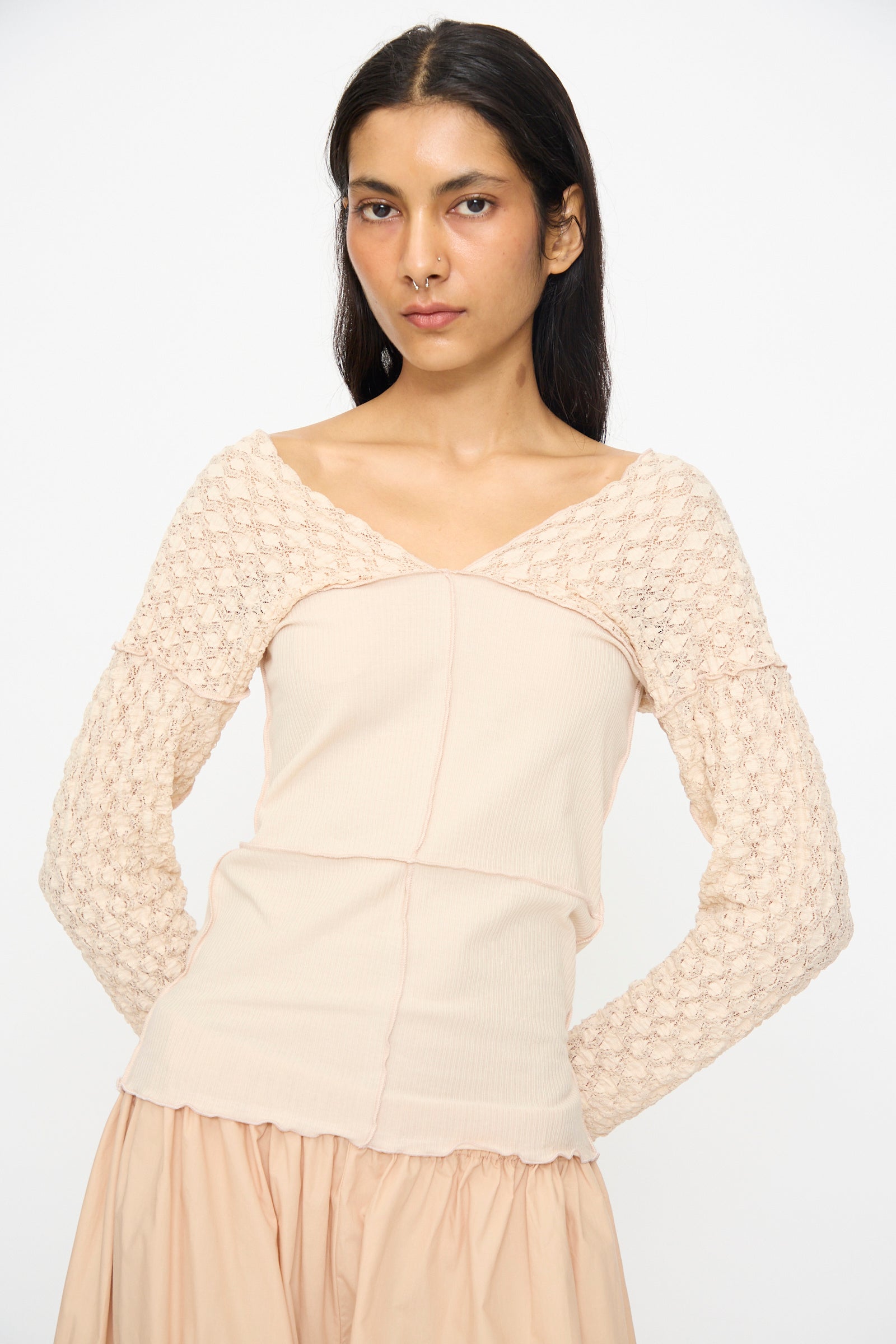 Woman with long dark hair wears the Baserange Nehru Long Sleeve Tee in Dylan Beige, a slim fit ribbed cotton top with lace sleeves, paired with a matching skirt, standing against a plain white background.