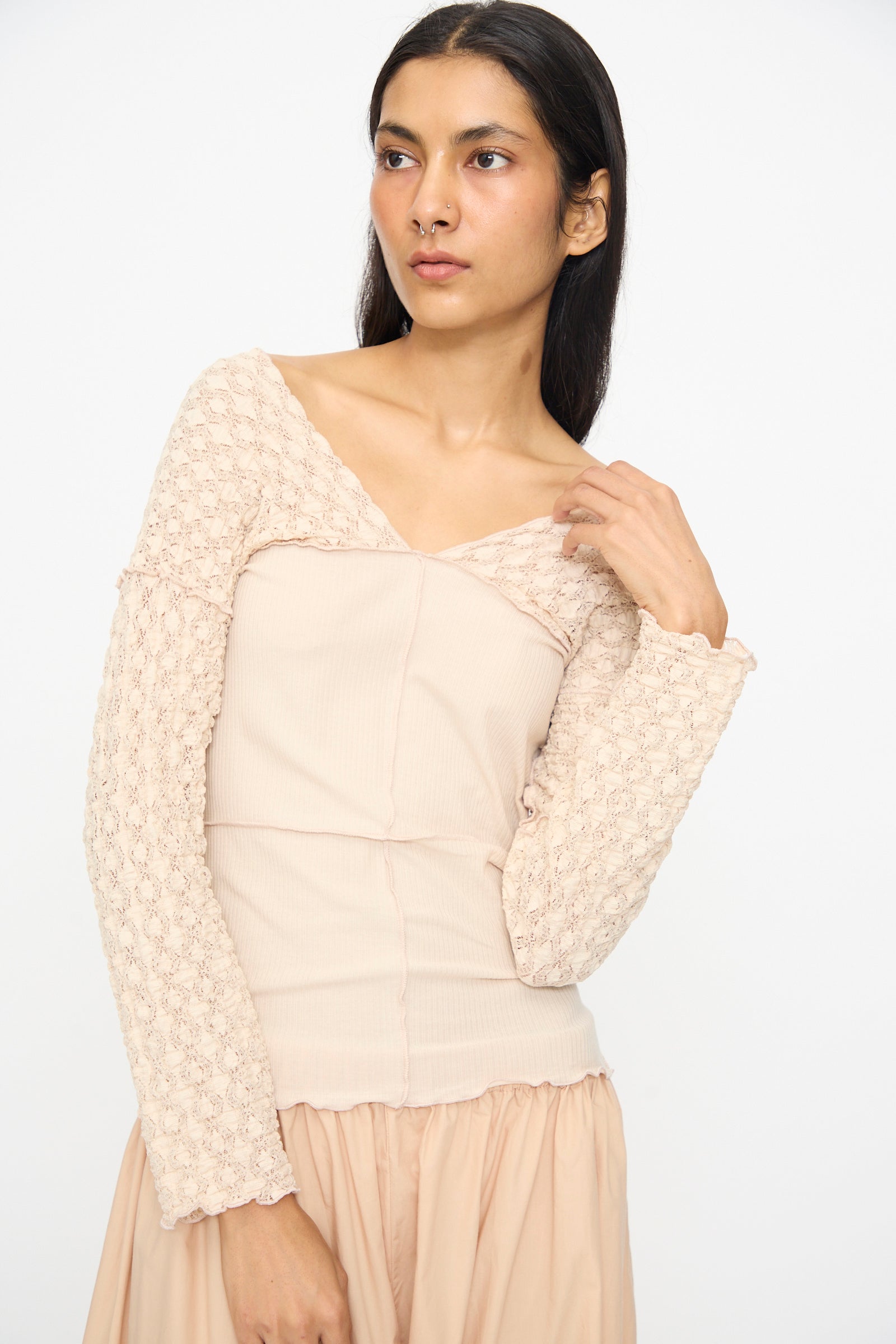 A woman with long dark hair poses against a plain background, wearing the Baserange Nehru Long Sleeve Tee in Dylan Beige paired with a matching skirt.