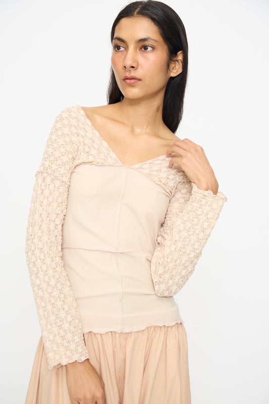 A woman with long dark hair poses against a plain background, wearing the Baserange Nehru Long Sleeve Tee in Dylan Beige paired with a matching skirt.