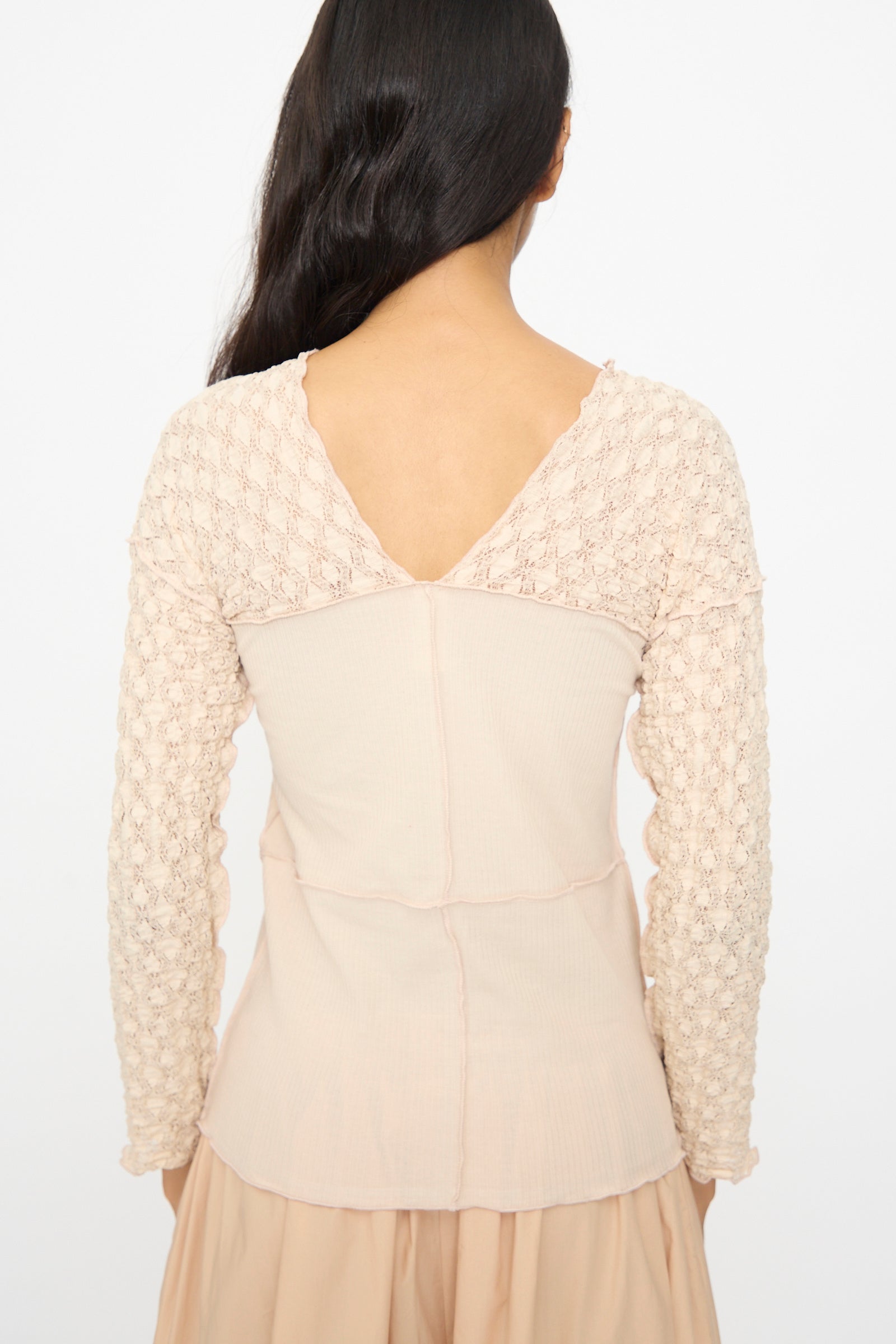 A woman with long dark hair, seen from behind, wears the Baserange Nehru Long Sleeve Tee in Dylan Beige against a plain background.