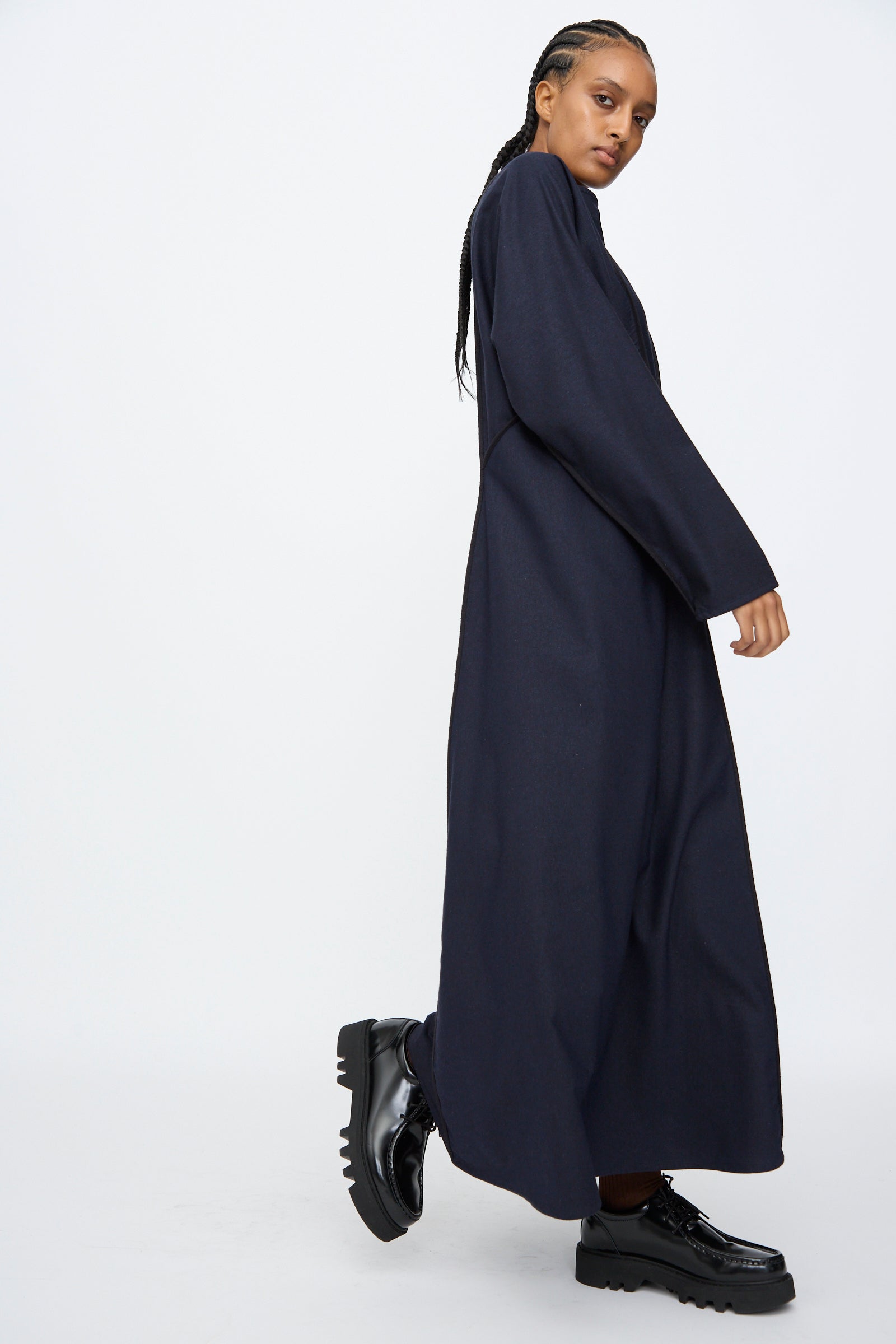 A person wearing the Baserange Nika Dress in Dama Navy stands against a plain white background, paired with chunky black platform shoes.
