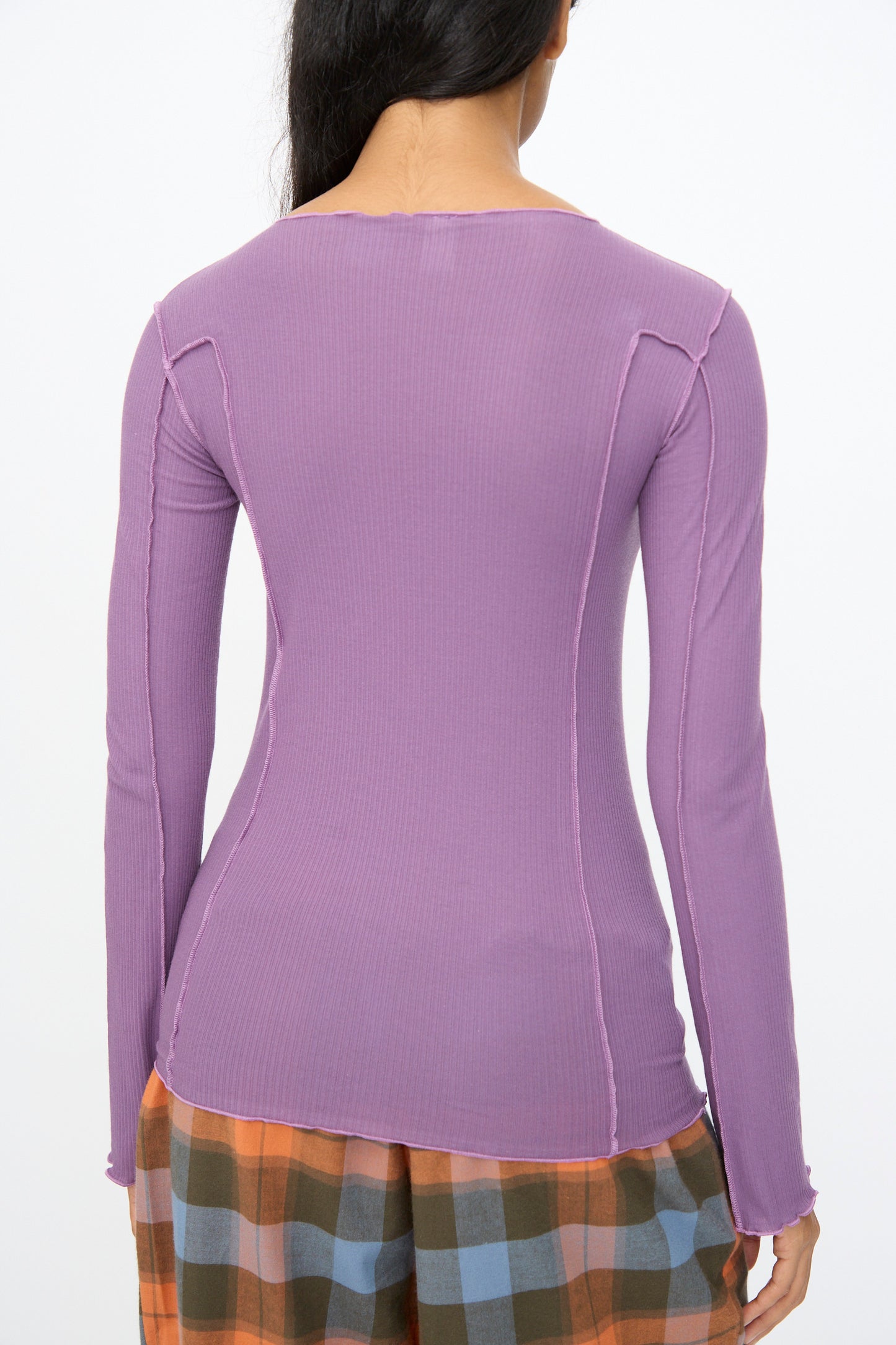 A person shown from the back wearing the Baserange Omato Long Sleeve Tee in Venet Purple and orange, green, and blue plaid pants.