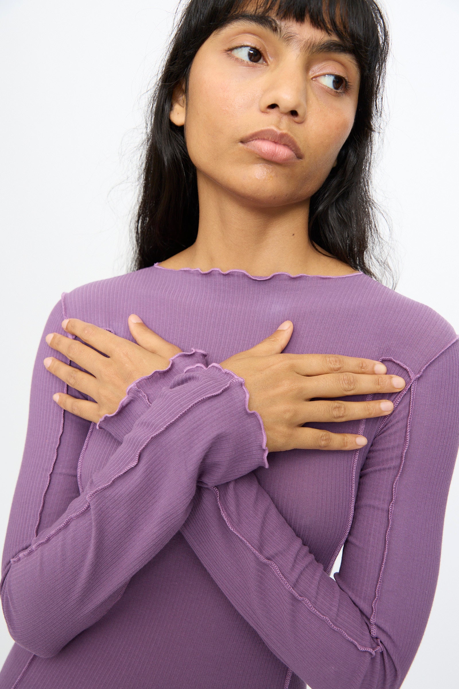 A person wears the Baserange Omato Long Sleeve Tee in Venet Purple, standing with arms crossed and looking slightly away from the camera.