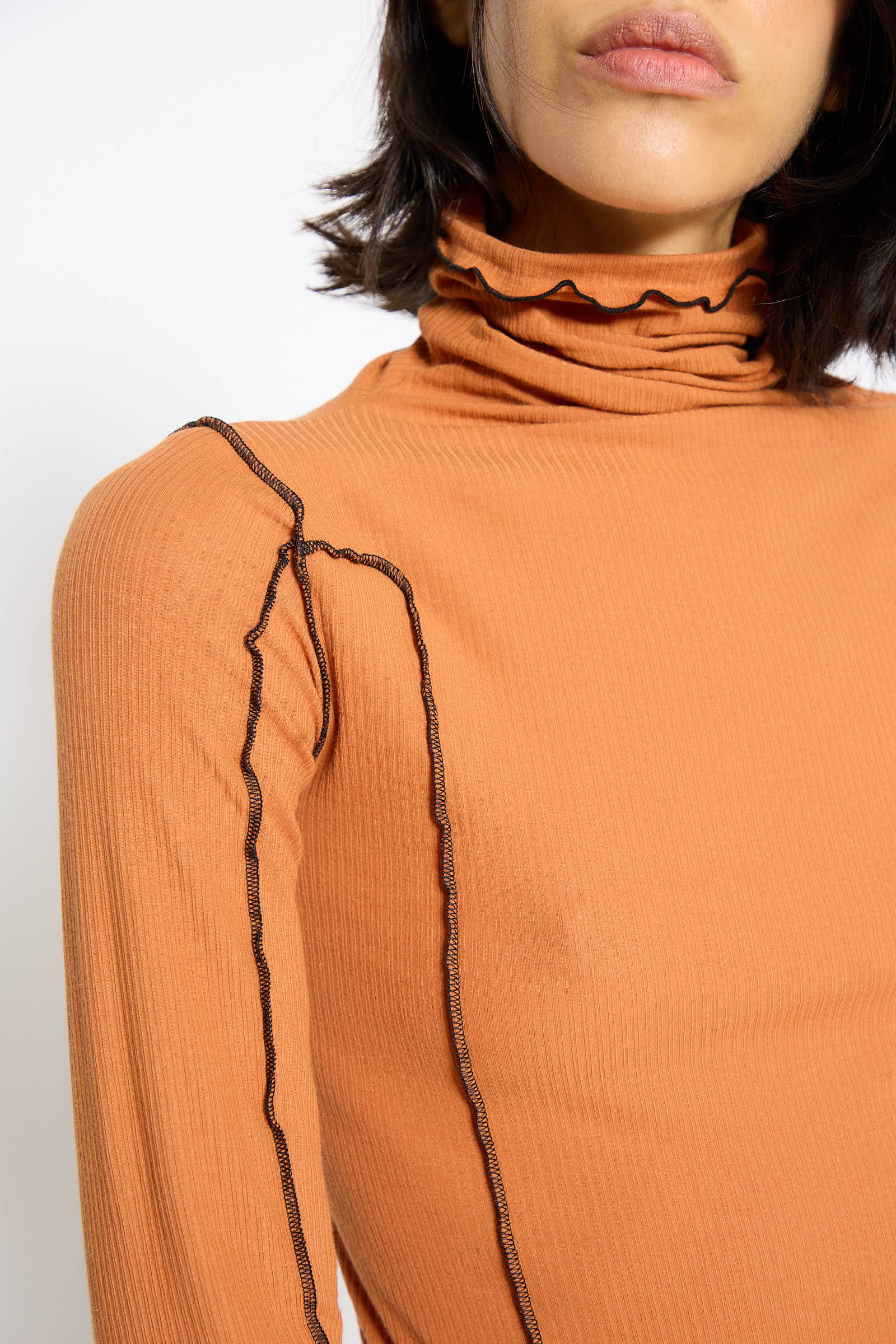 A person is wearing the Omato Turtleneck in Dre Orange by Baserange, featuring ruffled edges and visible seams, made from organic cotton. The focus is on the upper torso and neck.