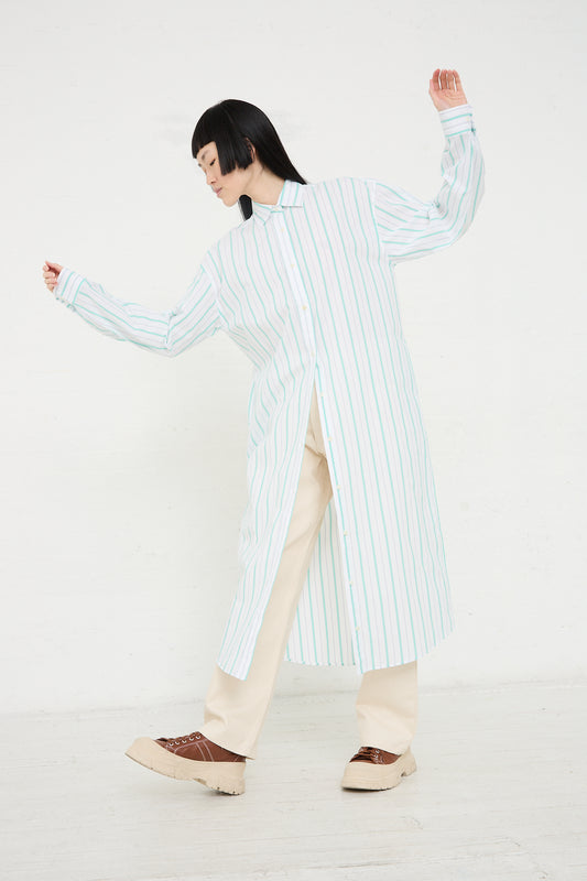 A person in a Baserange Organic Cotton Ole Shirt Dress in Stripe and light trousers, both sustainably produced from organic cotton, striking a dynamic pose against a white background.